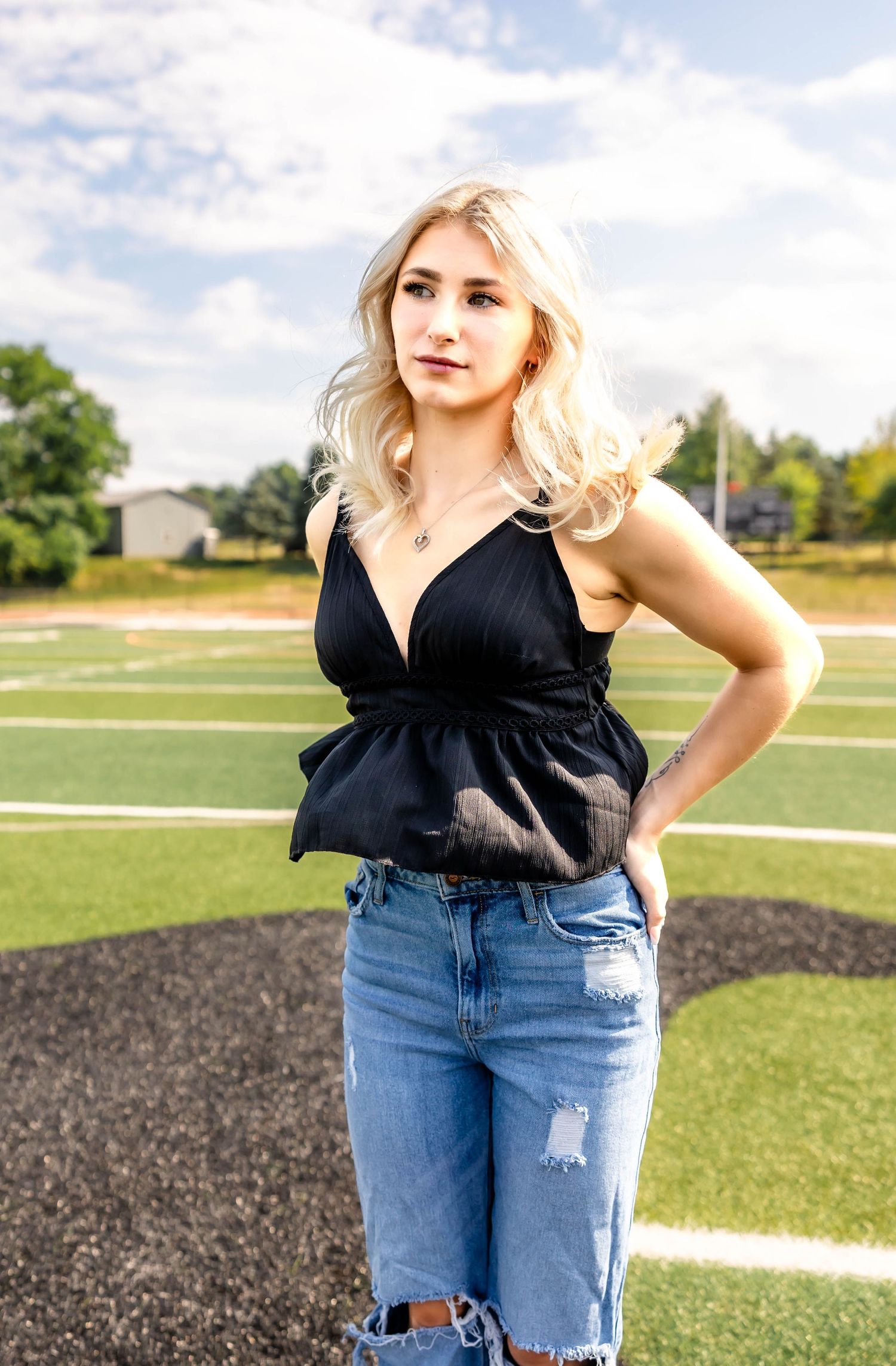 Fashion portrait on a sports field featuring a black peplum tank top and distressed denim.