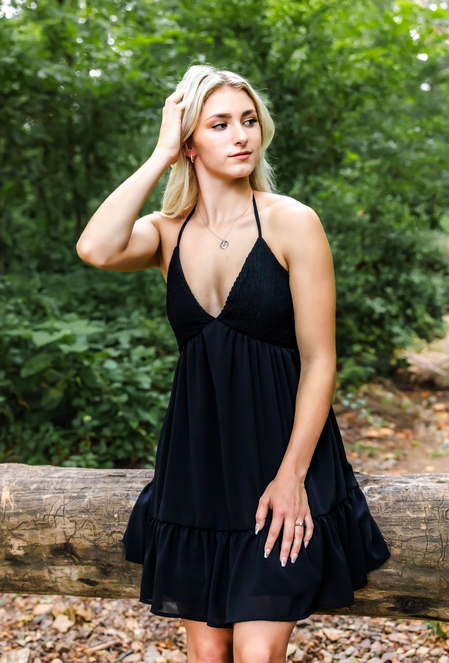 A casual black summer dress displayed in a natural forest setting with fallen logs.