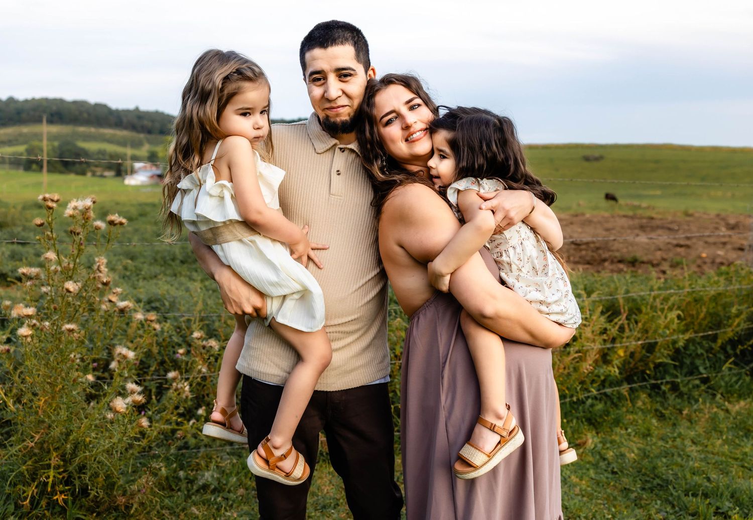 Family of four poses together in pastoral setting with rolling hills in background.