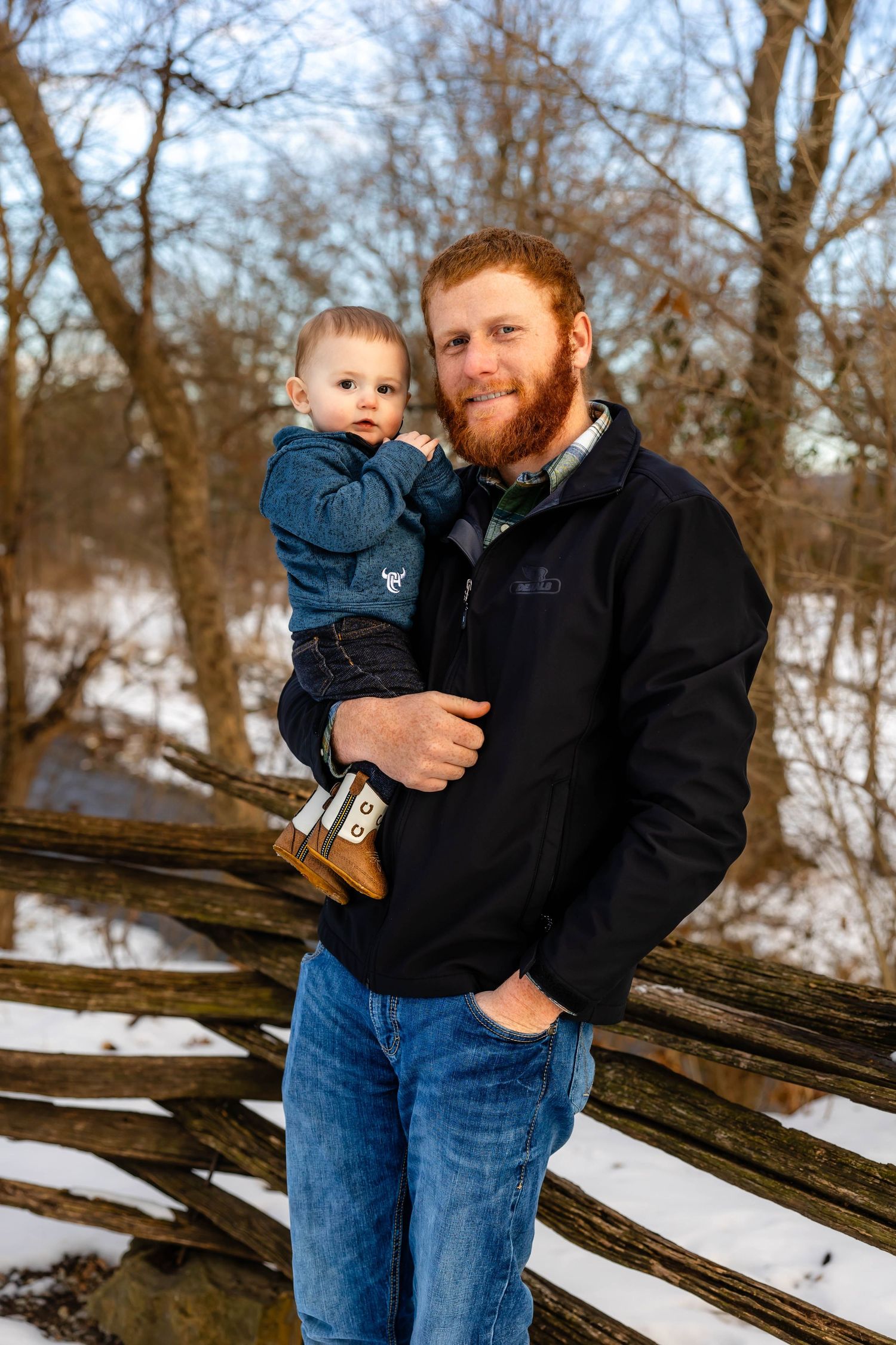 Father and young child pose together by rustic fence during winter photo session.