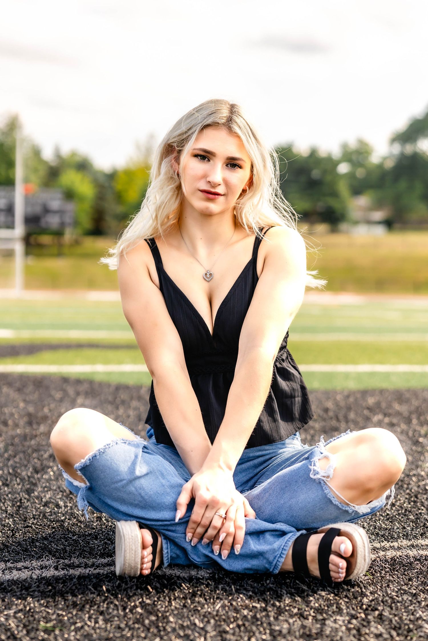 Casual summer style with black peplum tank and distressed jeans on athletic track surface.