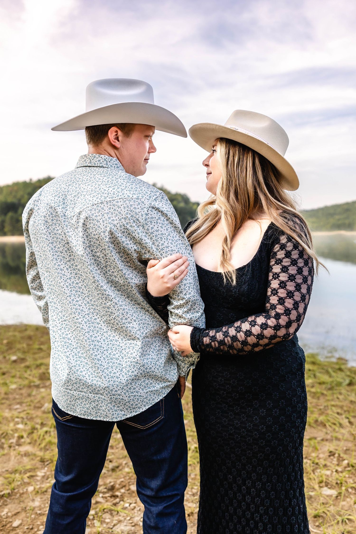 Intimate portrait of a couple in cowboy hats and formal wear standing by a lake.