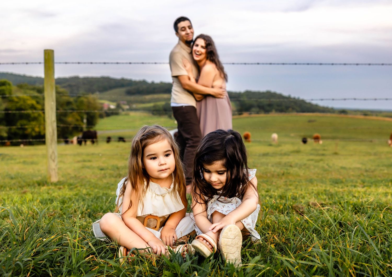 A family portrait composition on rolling farmland with a barbed wire fence and grazing cattle in background.