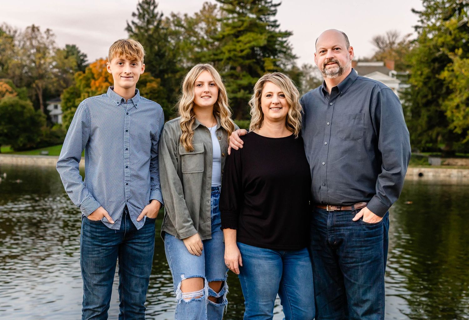 A family portrait taken by a lake with trees in the background during autumn.