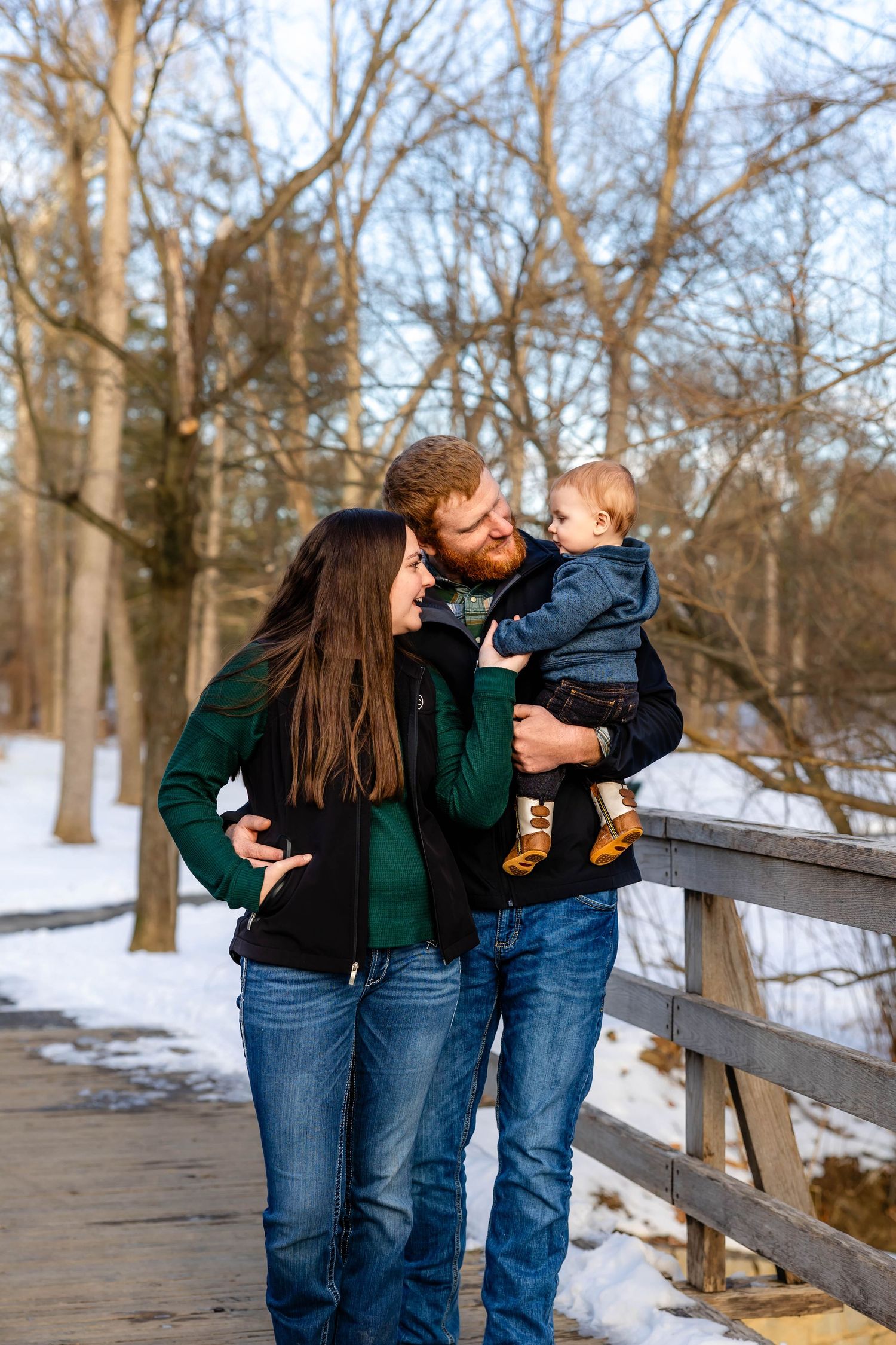 Intimate family portrait on wooden bridge surrounded by snow-covered winter scenery.