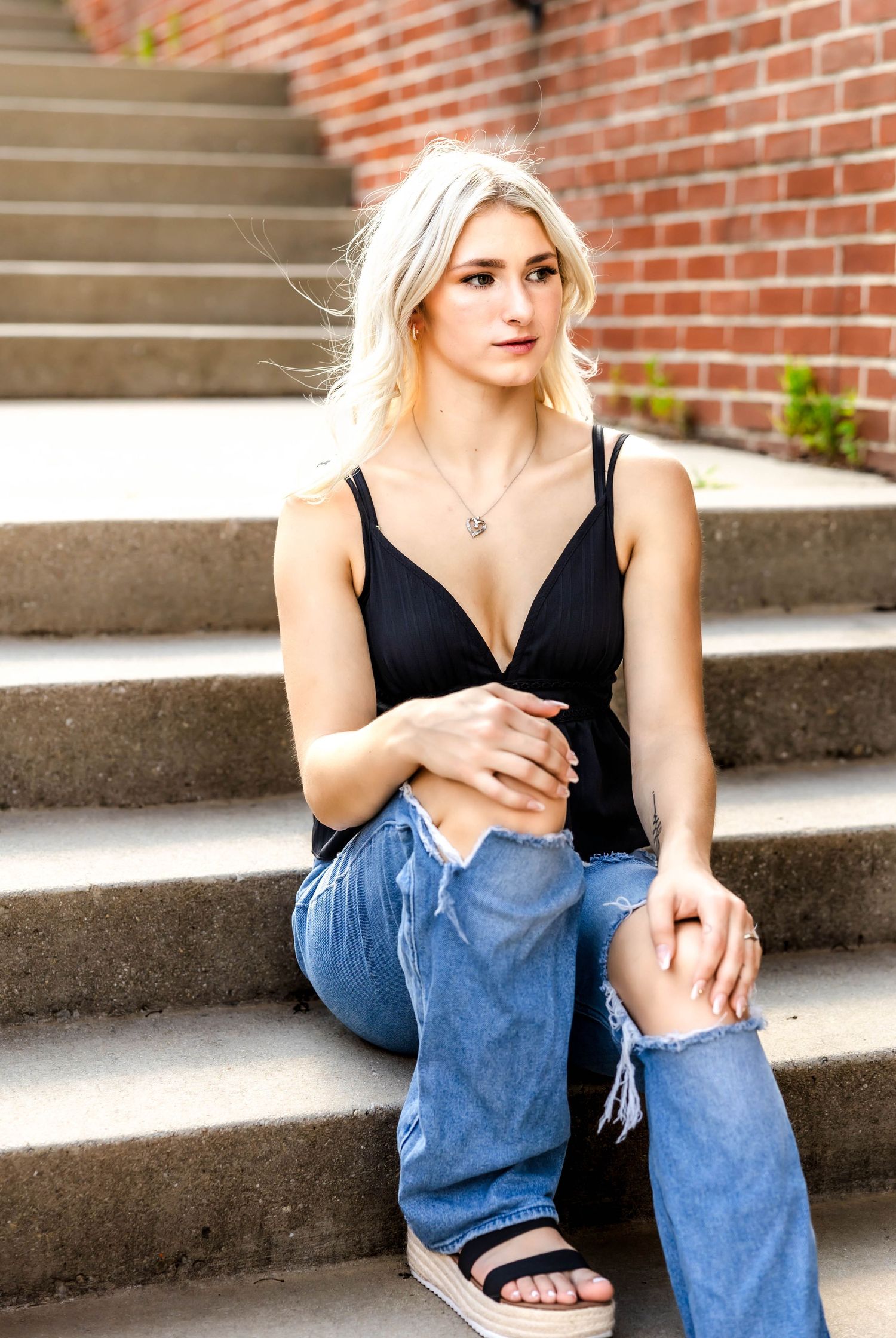 Fashion portrait on concrete steps against brick wall shows casual summer style.