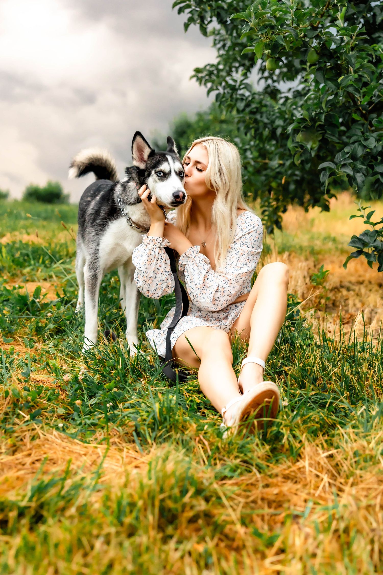 Woman in lace dress sitting on grass with friendly Husky dog in outdoor portrait.