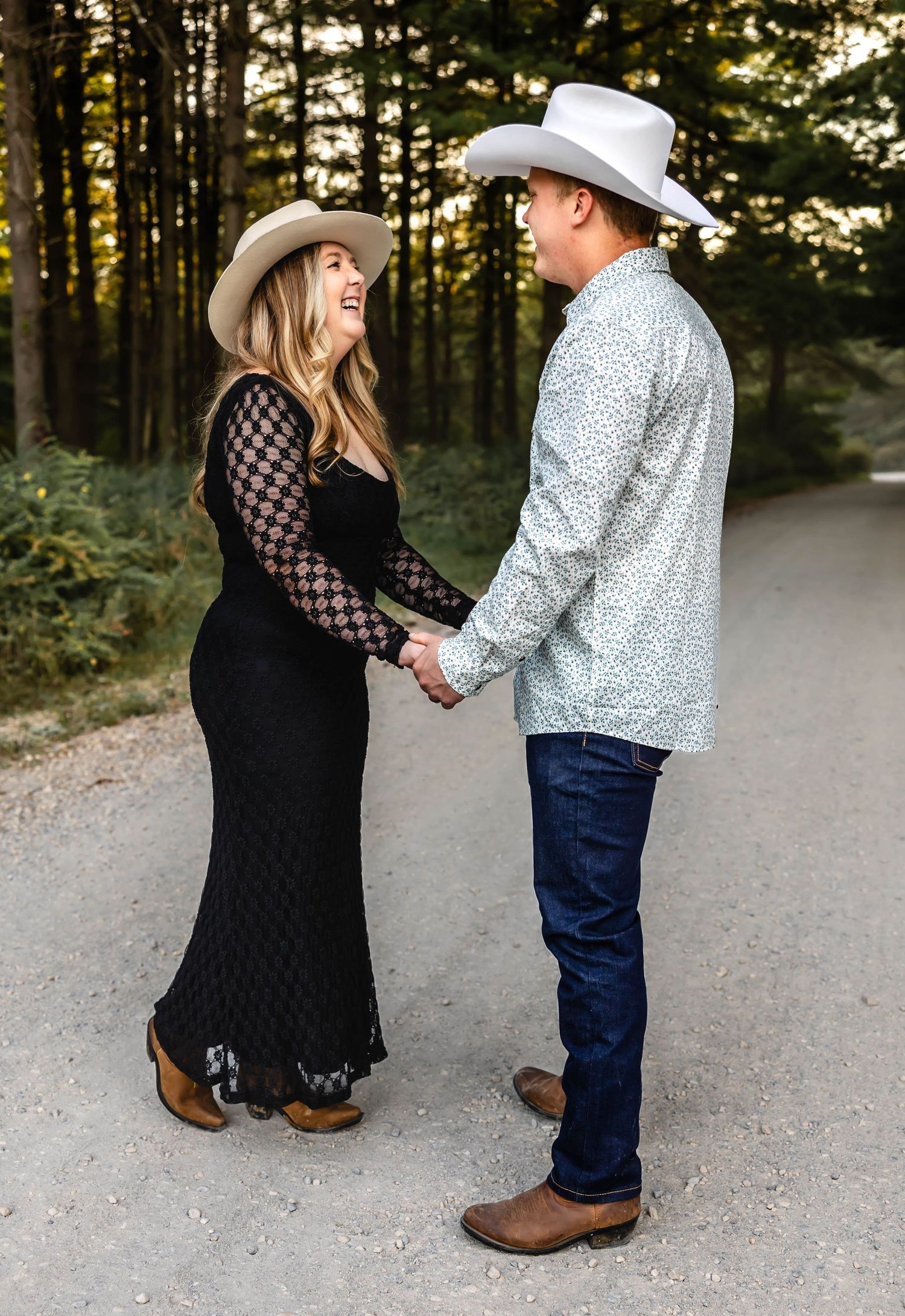 A romantic couple in cowboy hats share a tender moment on a forest trail at sunset.