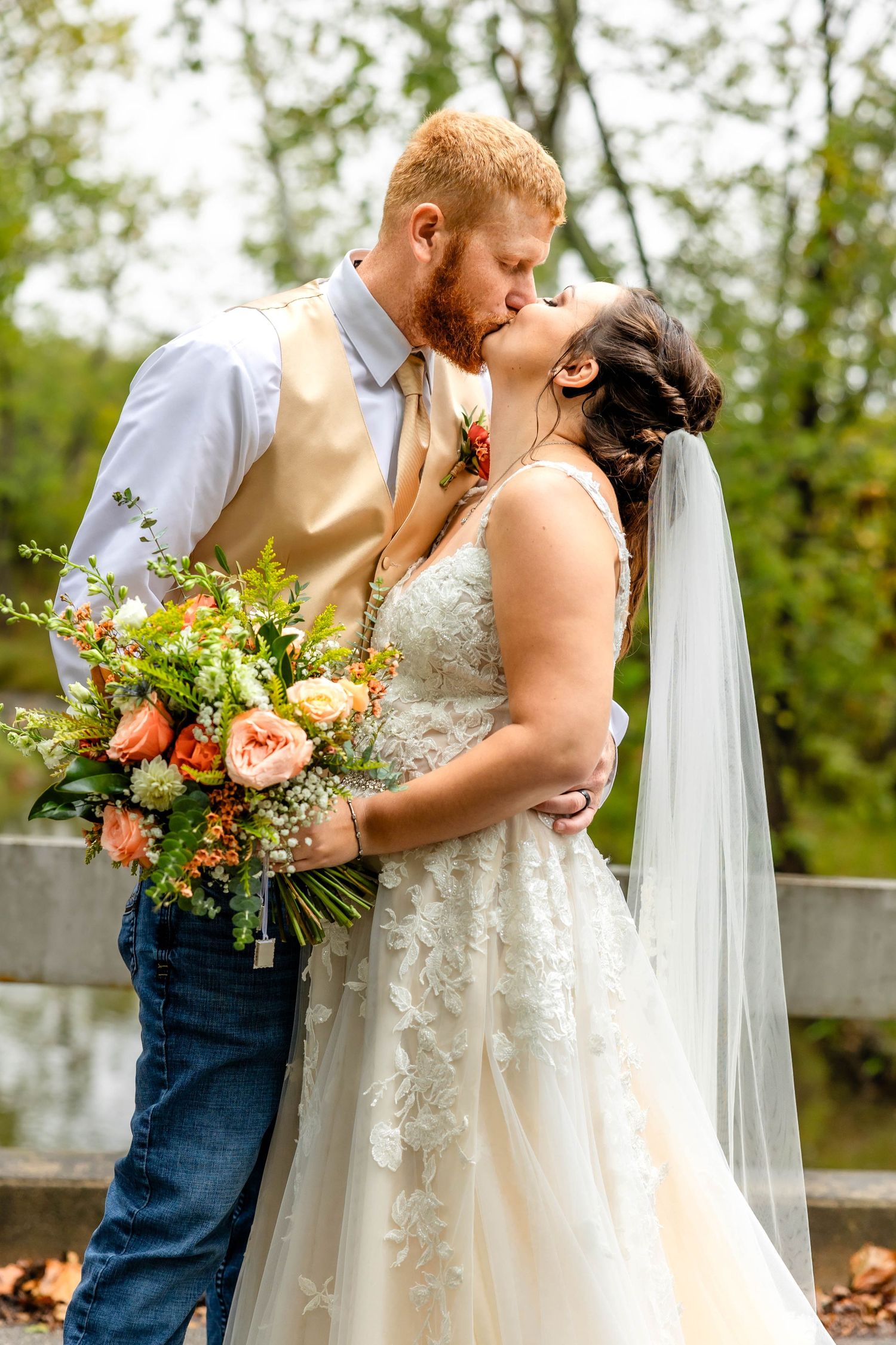 Bride and groom sharing kiss on wedding day with colorful fall bouquet.