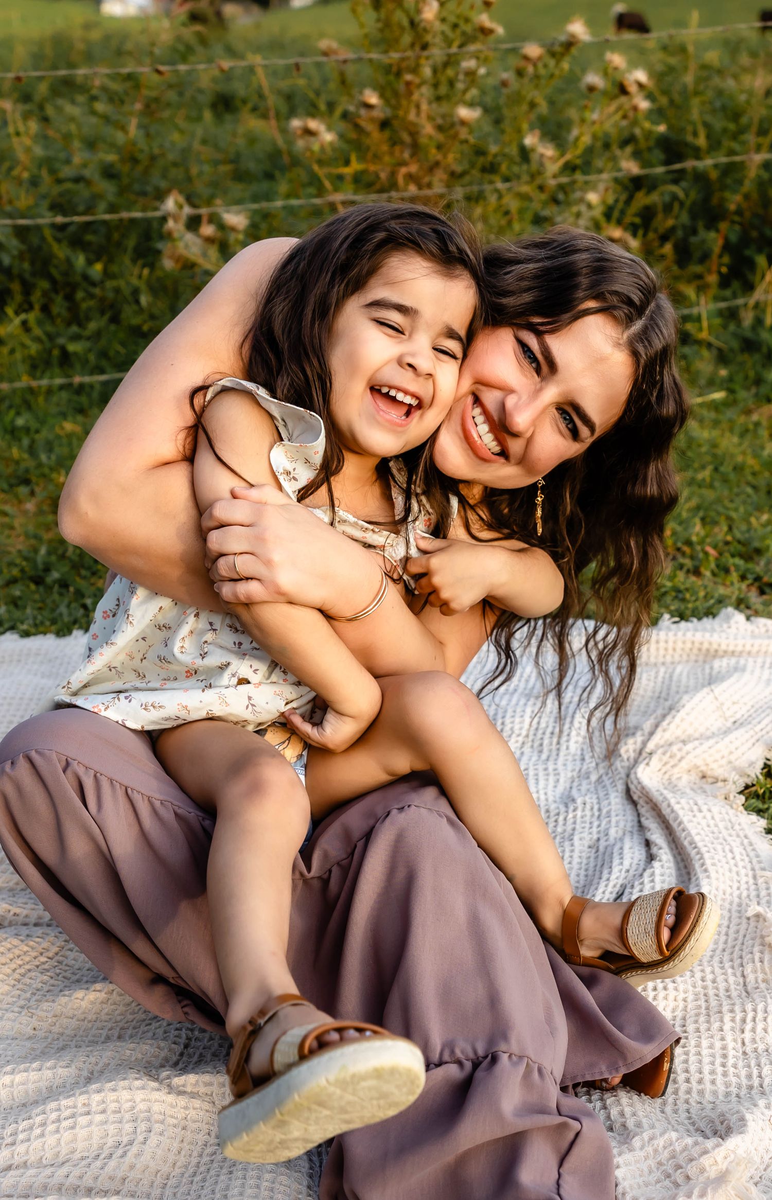 A joyful moment shared between parent and child laughing together on a picnic blanket outdoors.