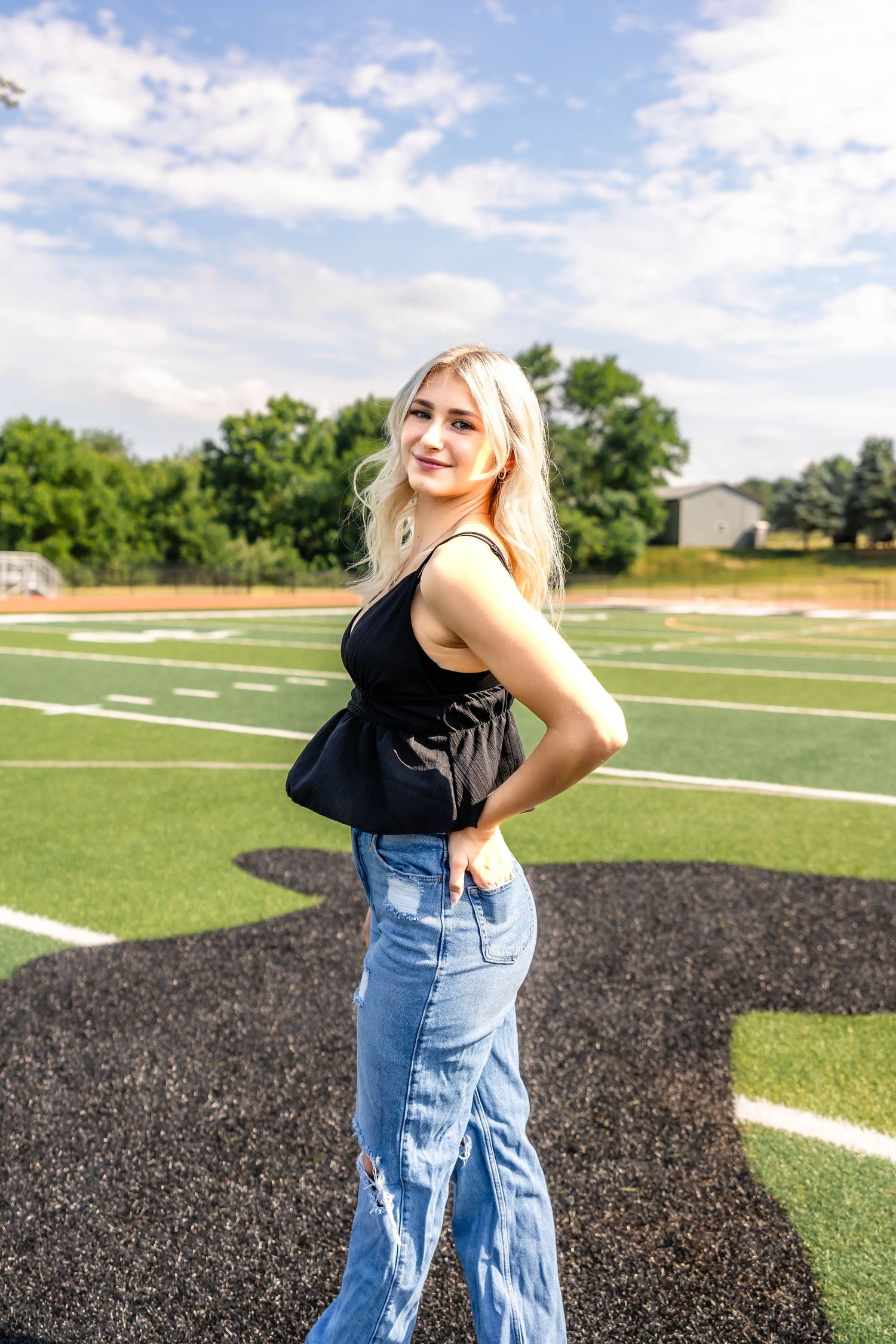 Summer fashion photography on a football field showcasing trendy casual wear against blue skies.