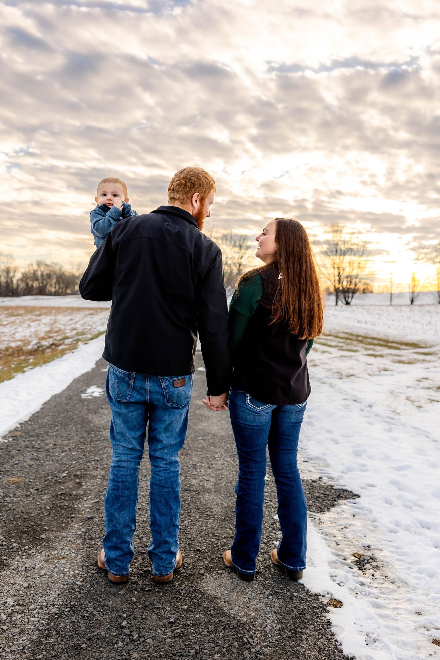 A family walks together on a snowy path during sunset with dramatic cloudy sky overhead.