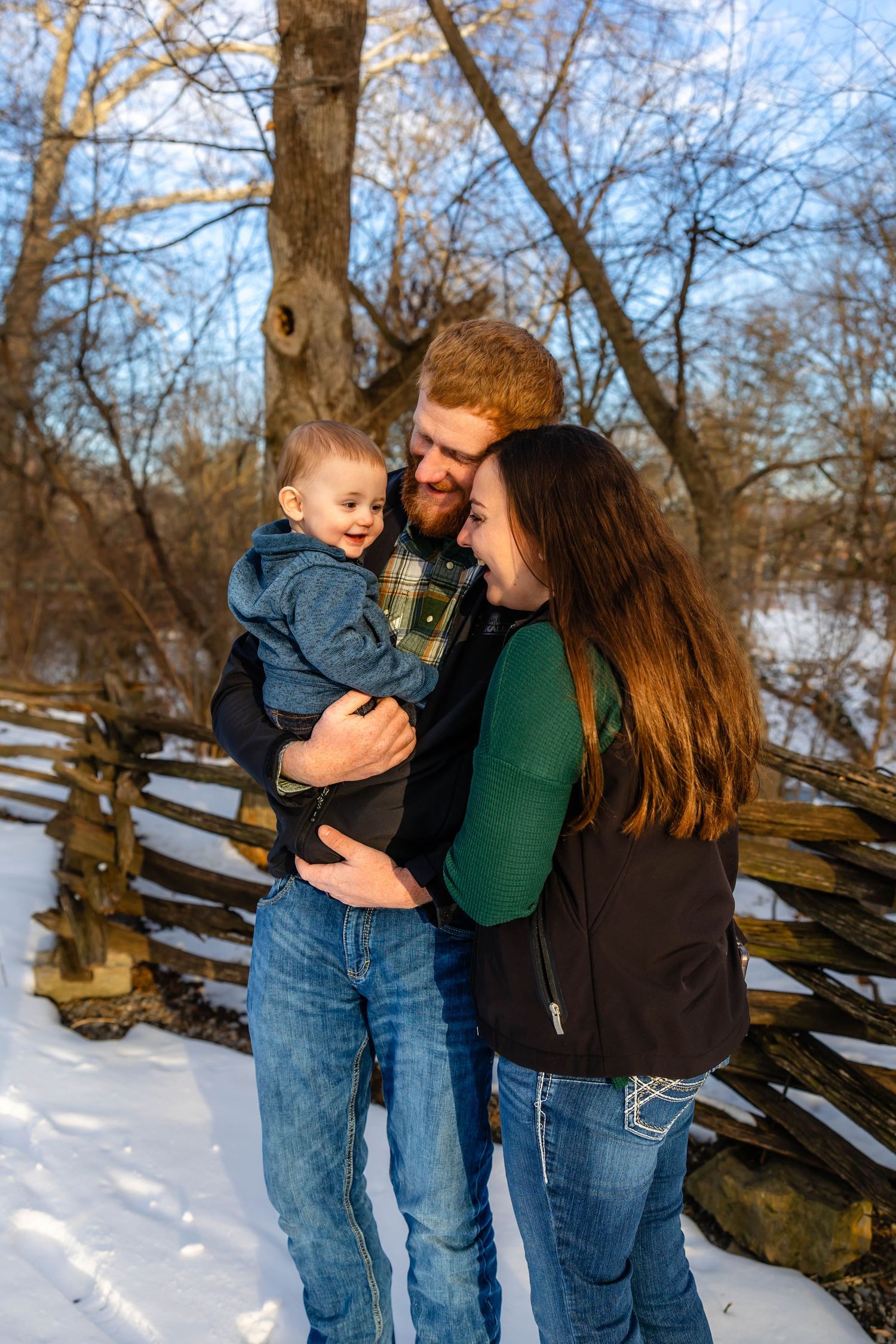 Candid family portrait in winter setting with rustic wood fence backdrop.