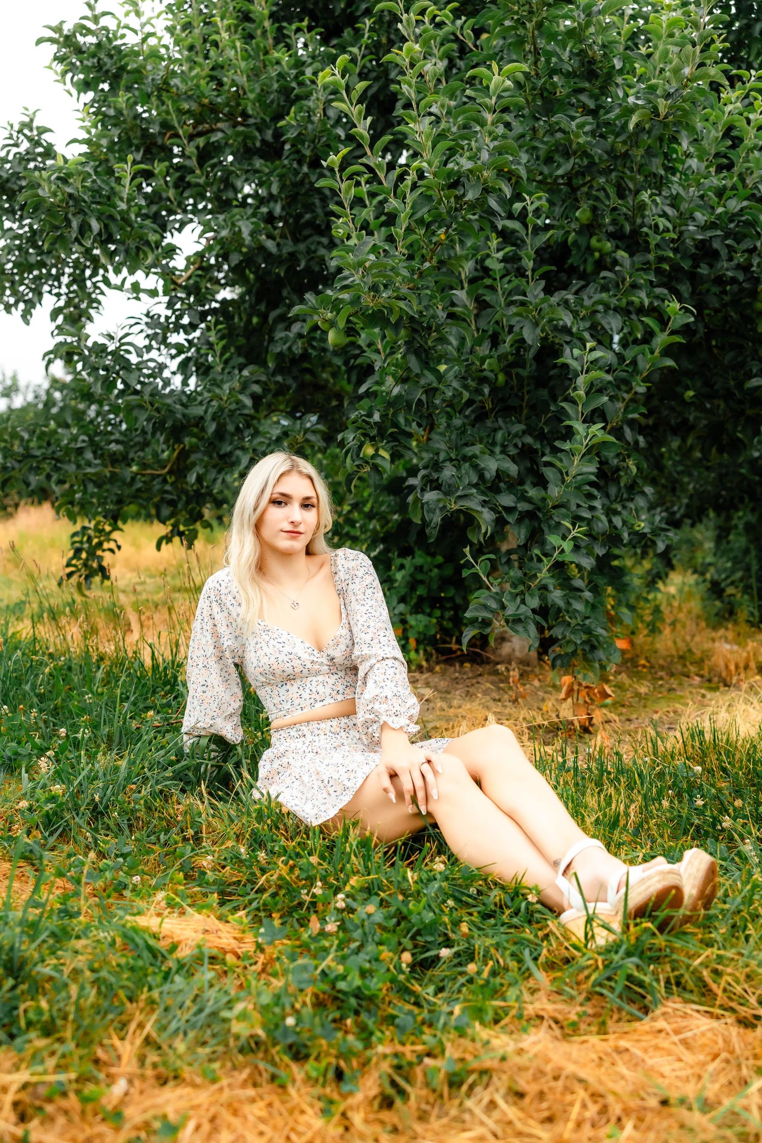 Casual summer fashion portrait in a white floral outfit sitting in an orchard.