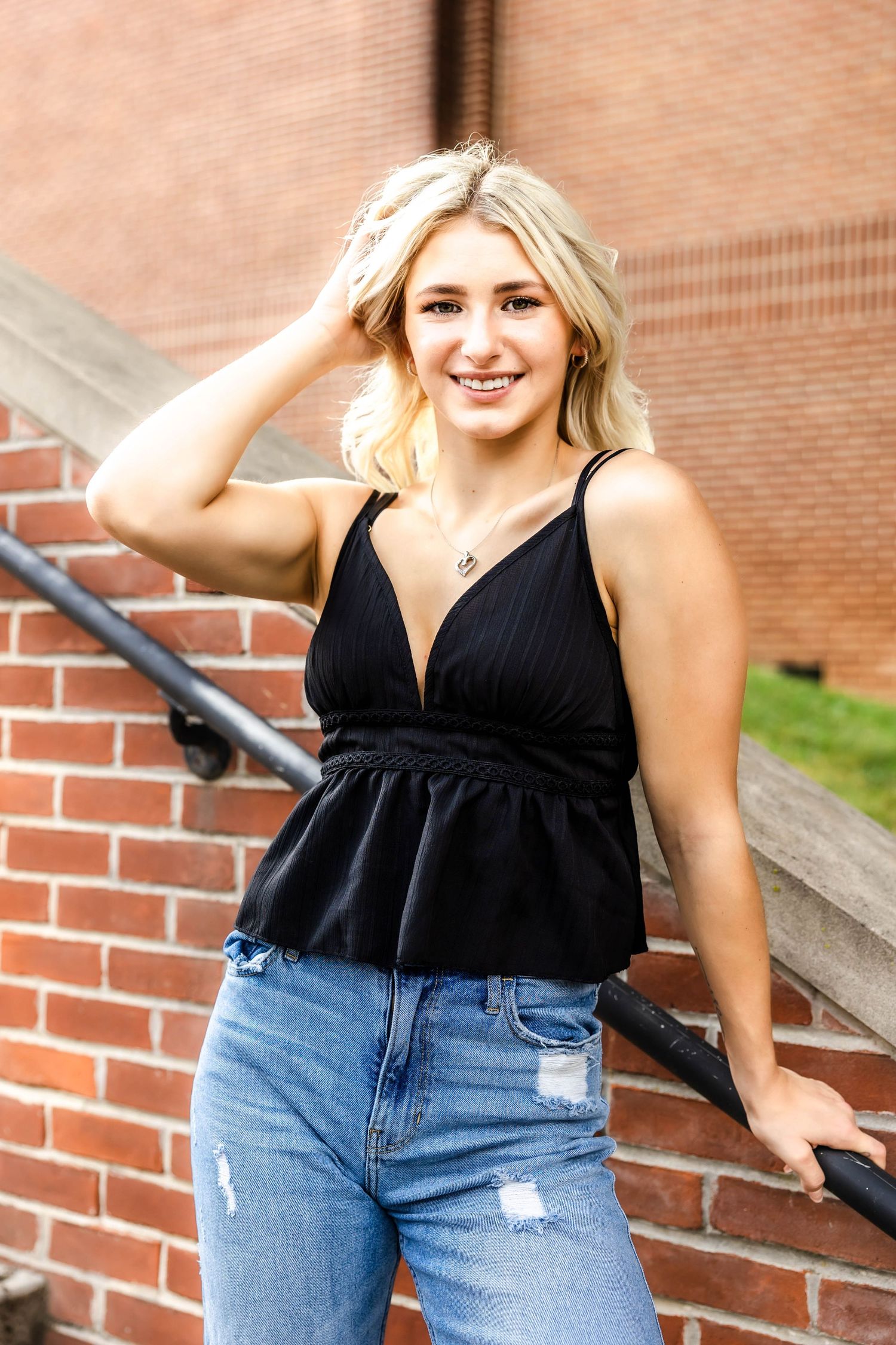 Casual summer look with black peplum top and distressed denim against brick architecture.