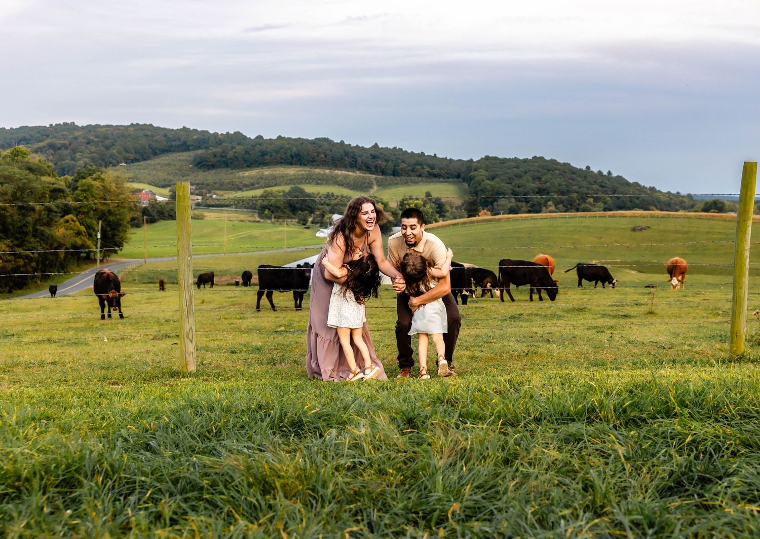 A joyful family moment captured in a scenic pasture with grazing cattle and mountains.