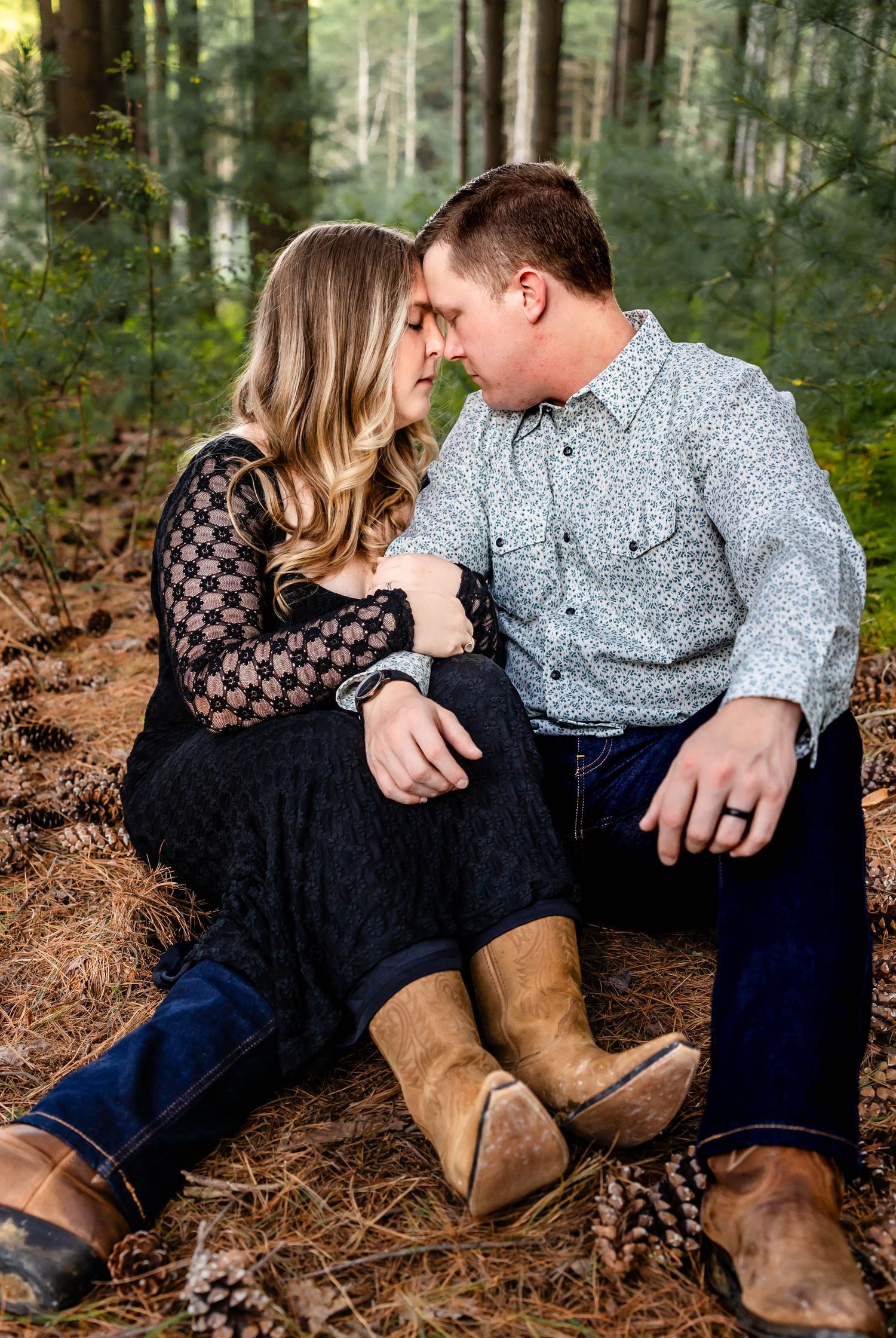 Intimate moment between couple wearing western-inspired outfits in forest setting.