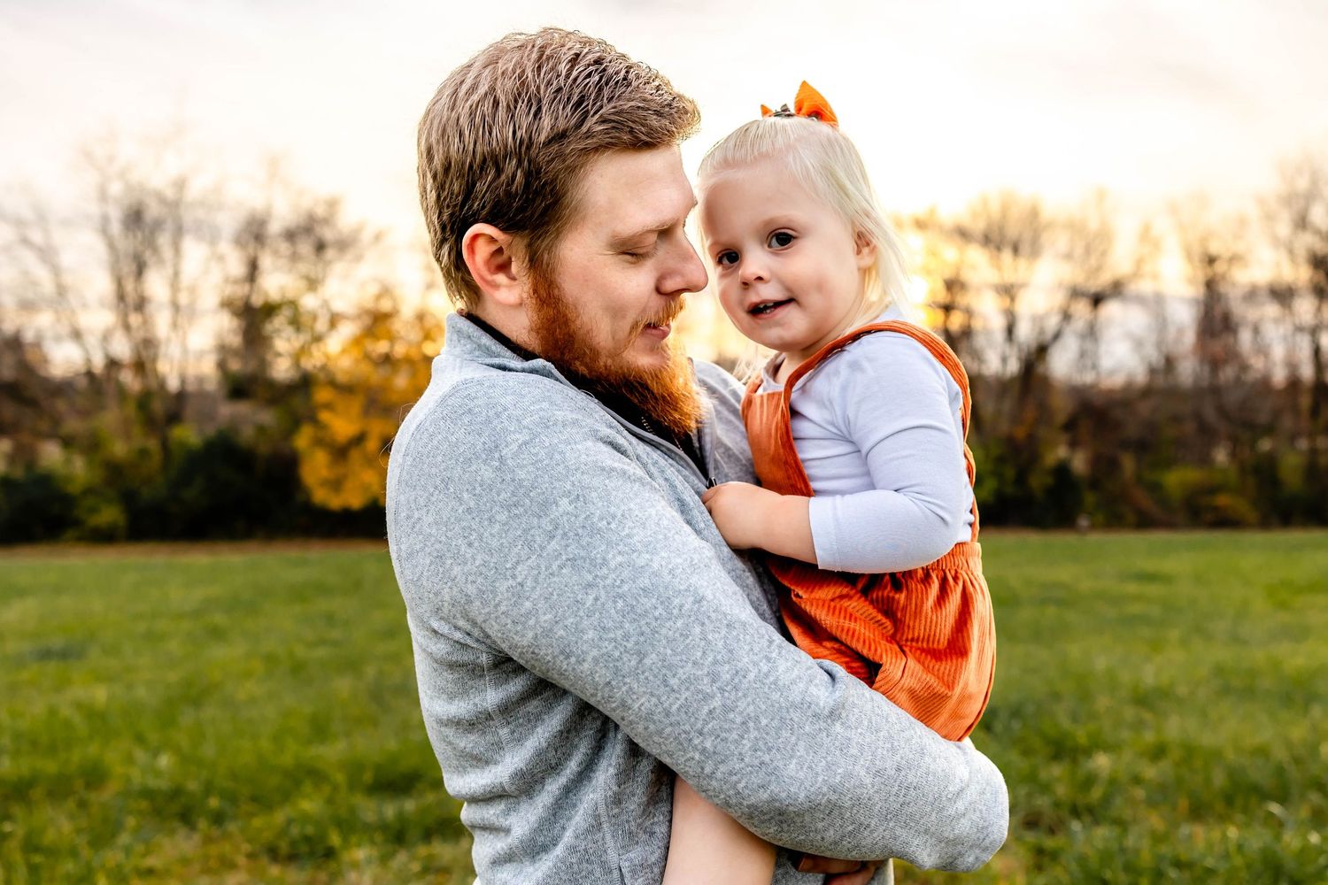 Joyful outdoor family portrait showing loving interaction against fall foliage backdrop.