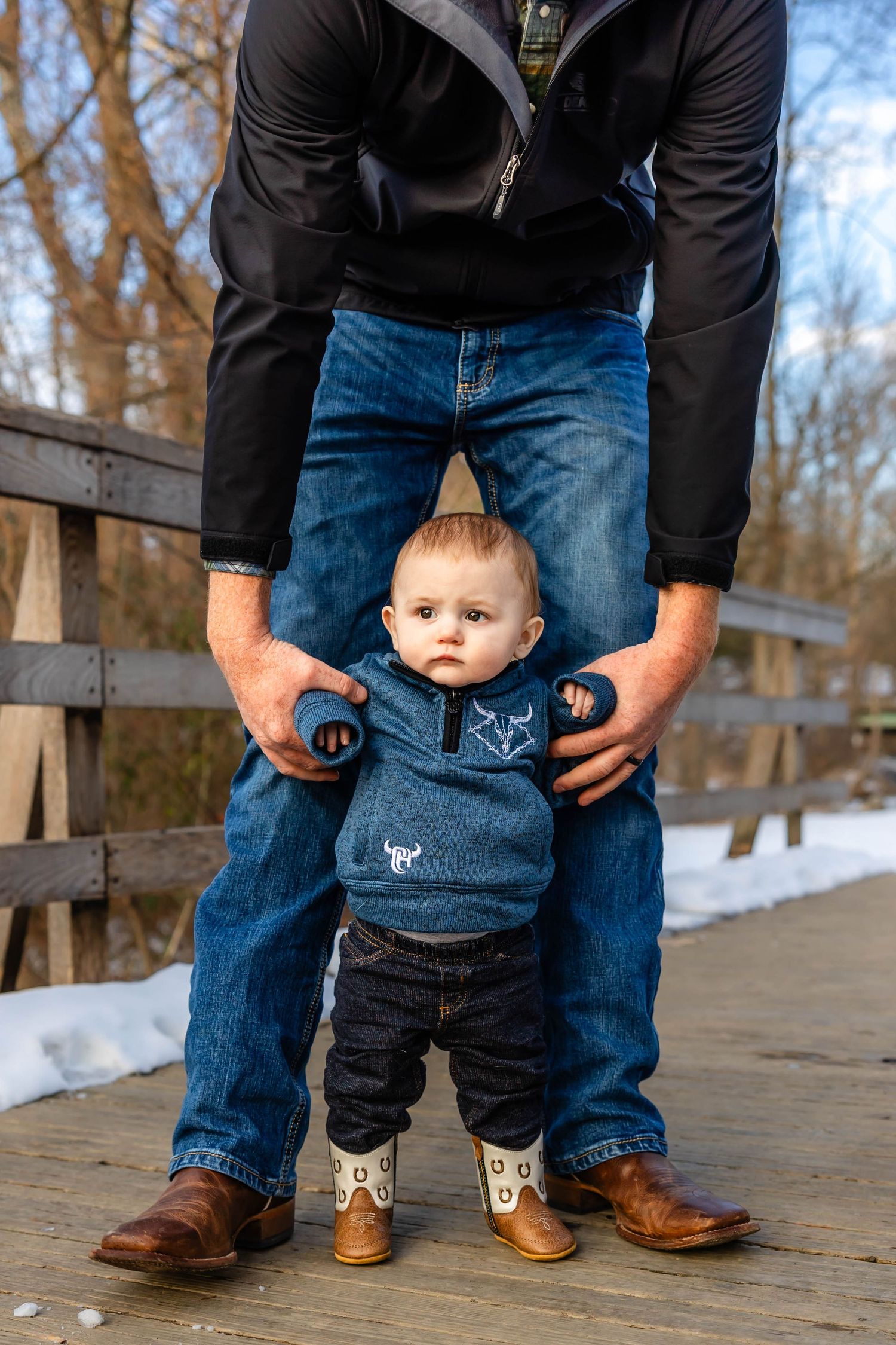 Toddler in blue sweater standing with support on wooden boardwalk.