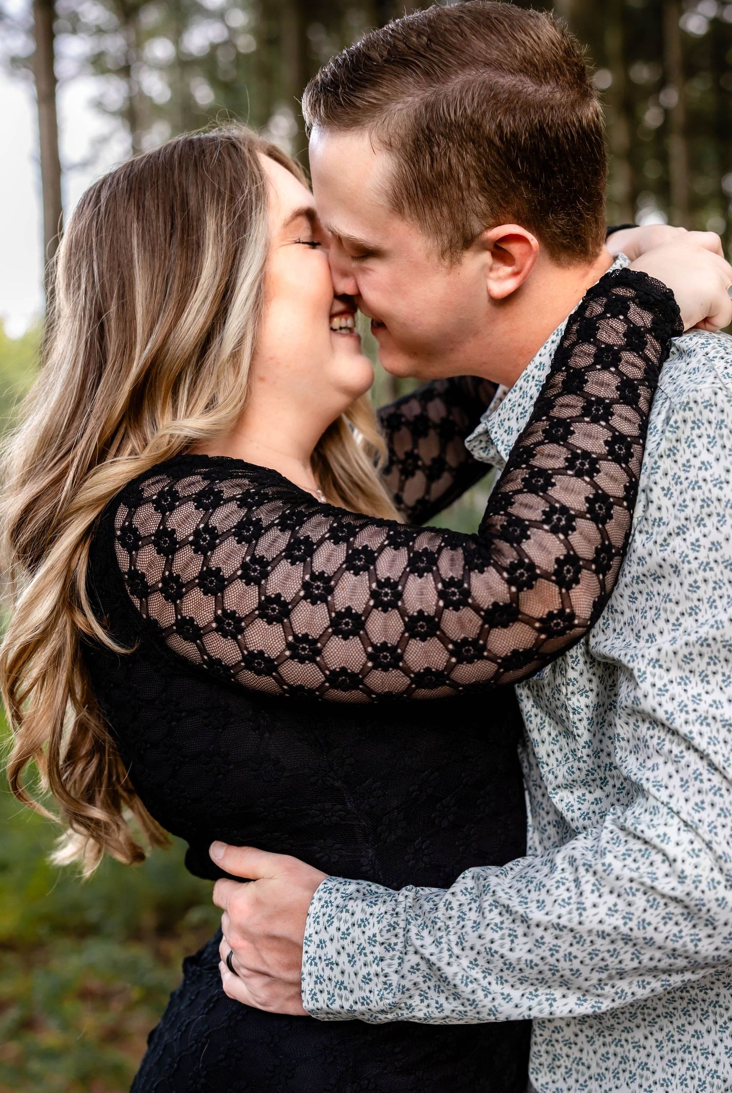 Joyful couple in contrasting black and gray outfits share a loving moment in the woods.