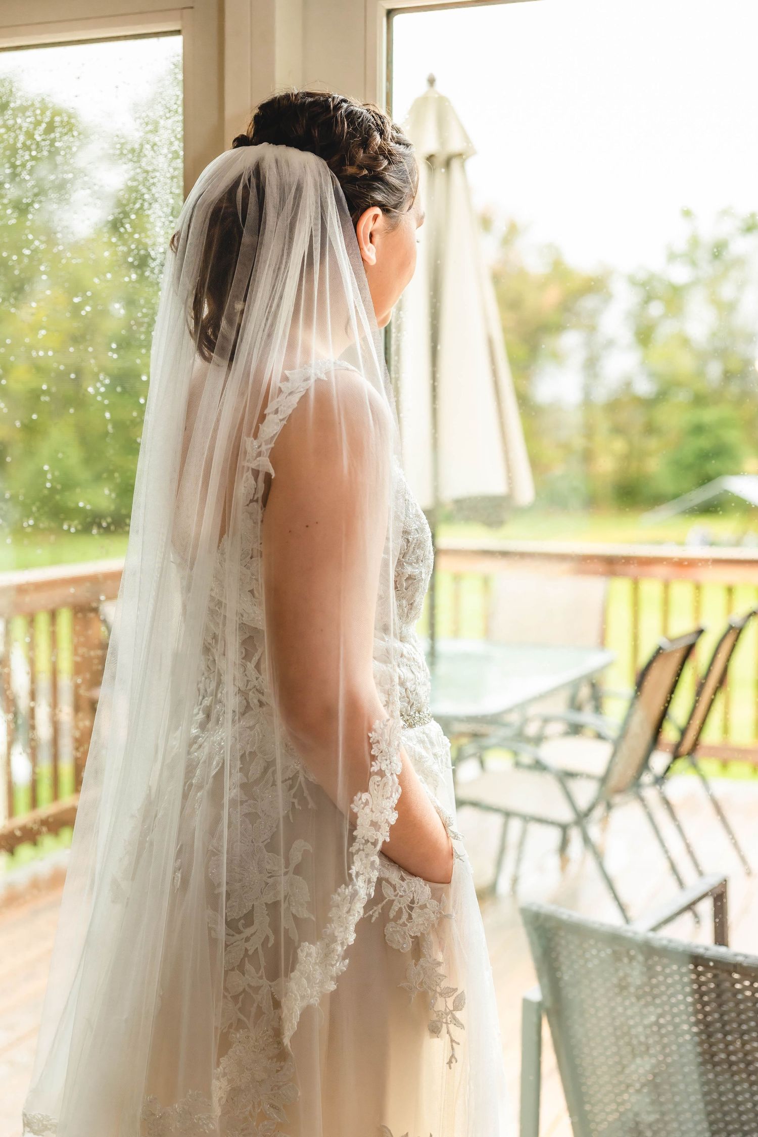 An elegant wedding dress with a long lace-trimmed veil captured from behind on a sunlit deck.