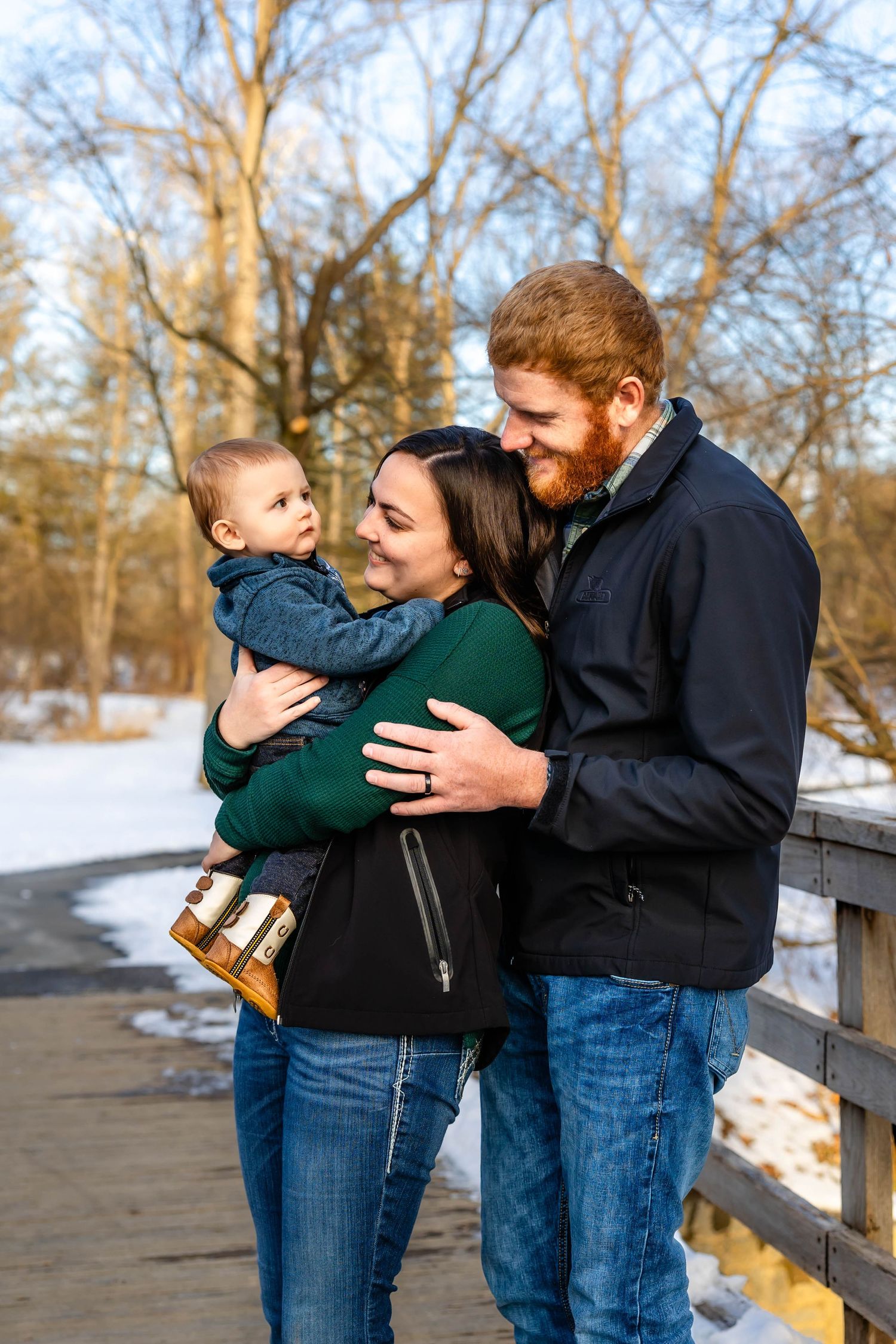 Loving family embrace captured on wooden bridge in snowy winter setting.