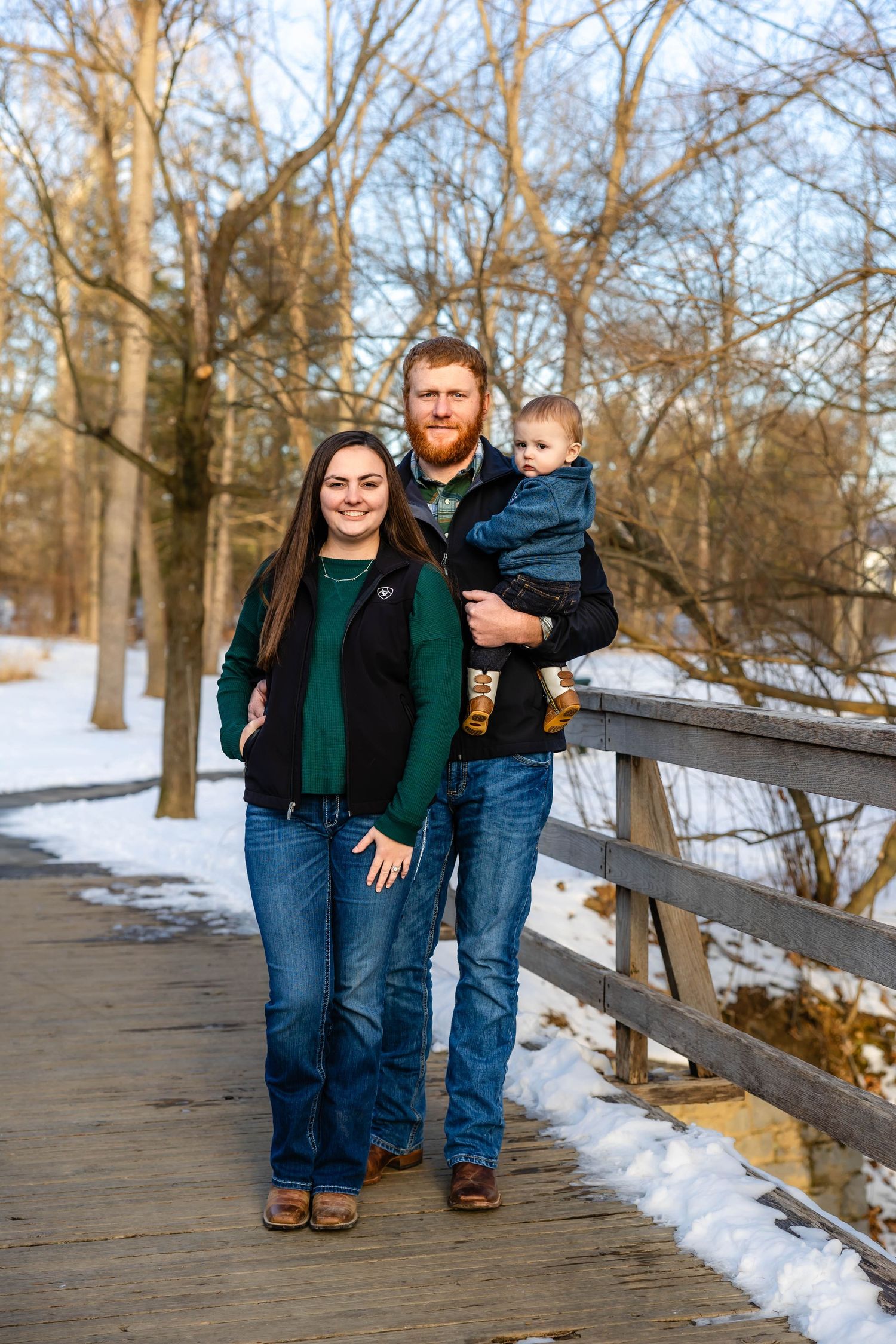 Family standing together on a wooden bridge in a snowy winter park landscape.