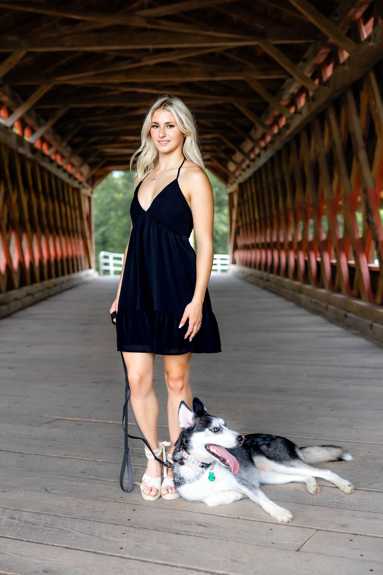 A black dress and husky dog posing together in a covered wooden bridge.