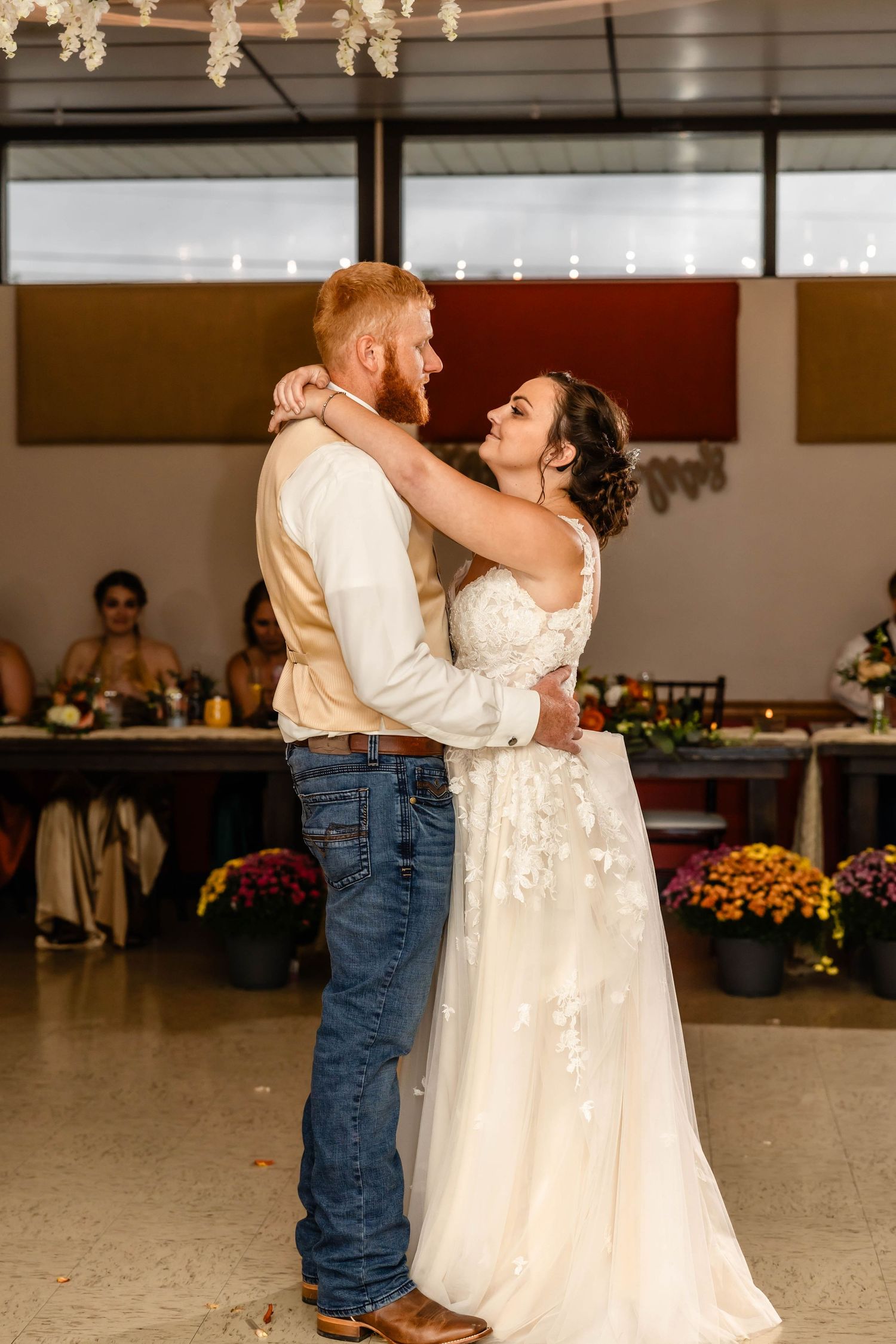 Couple shares an intimate dance moment in a reception hall decorated with floral arrangements.