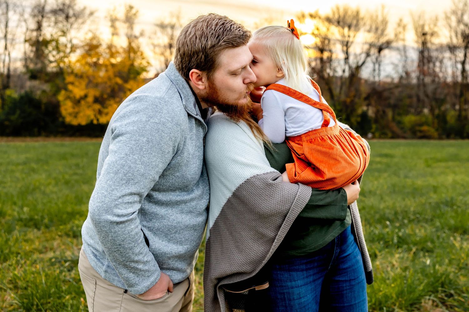 A family shares a tender moment together in an autumn field at sunset.