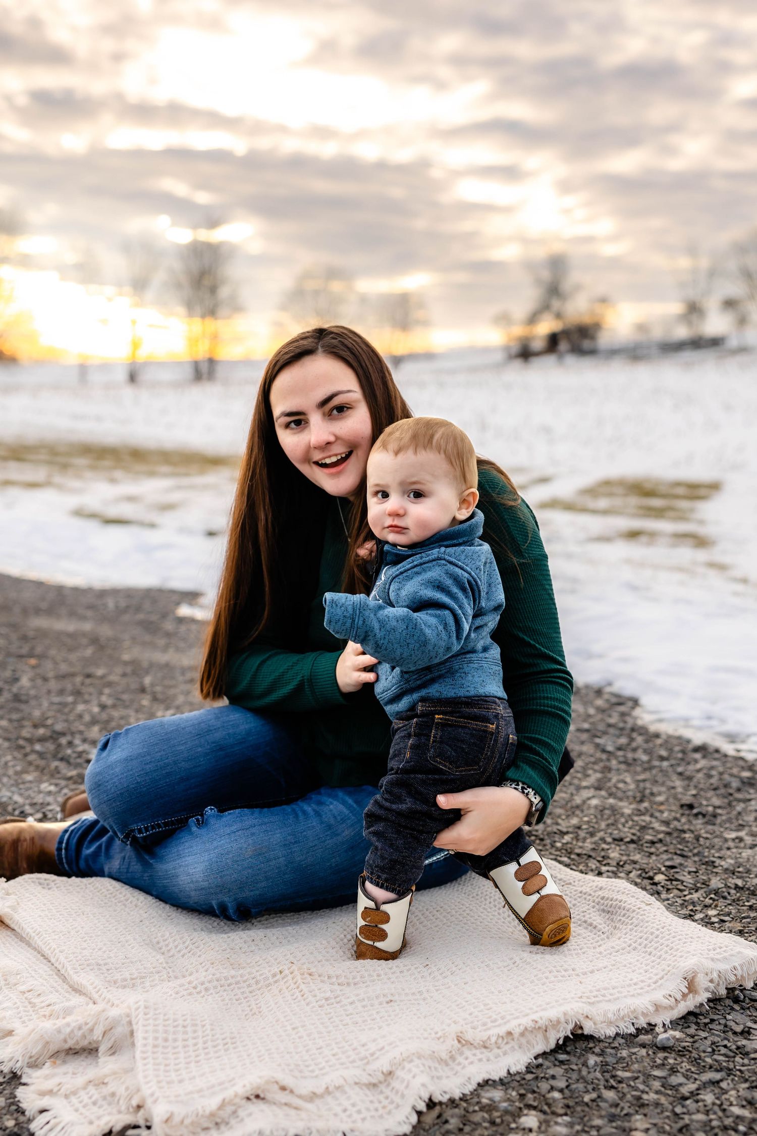 Loving outdoor portrait on a blanket with snow-covered fields and sunset in the background.