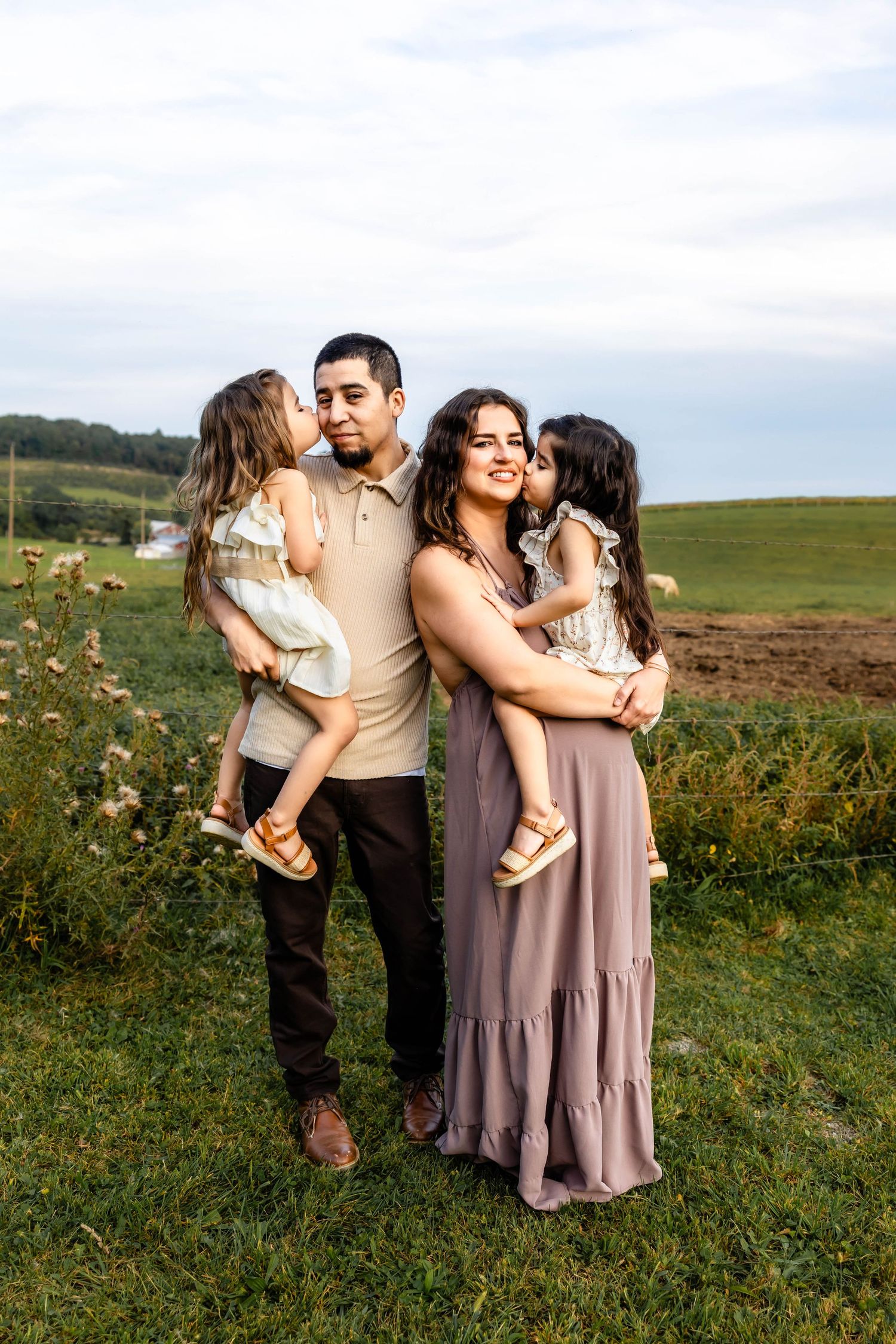 Family of four embracing in a green field during golden hour.