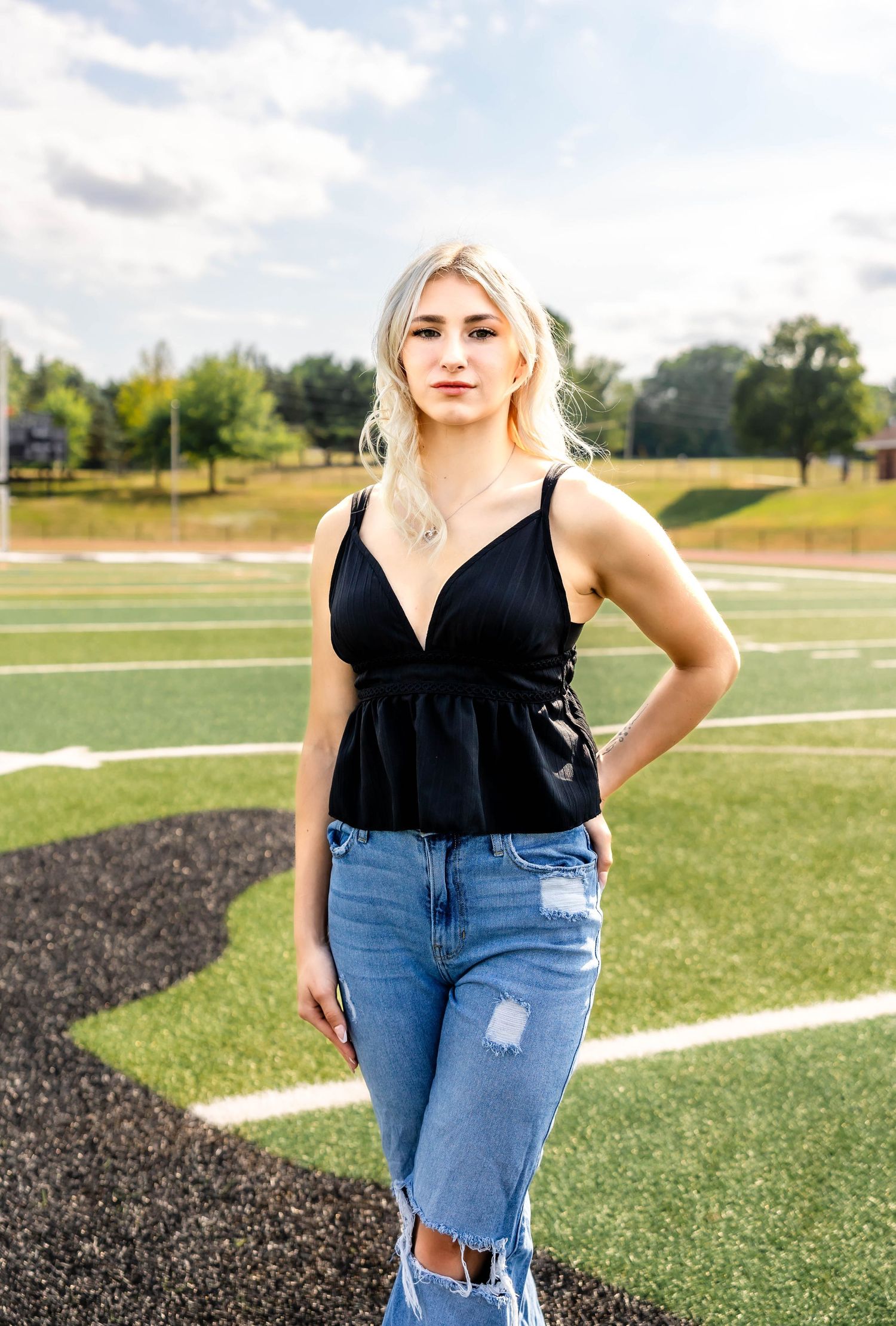Stylish casual outfit featuring a black v-neck top and ripped jeans photographed on an athletic field.