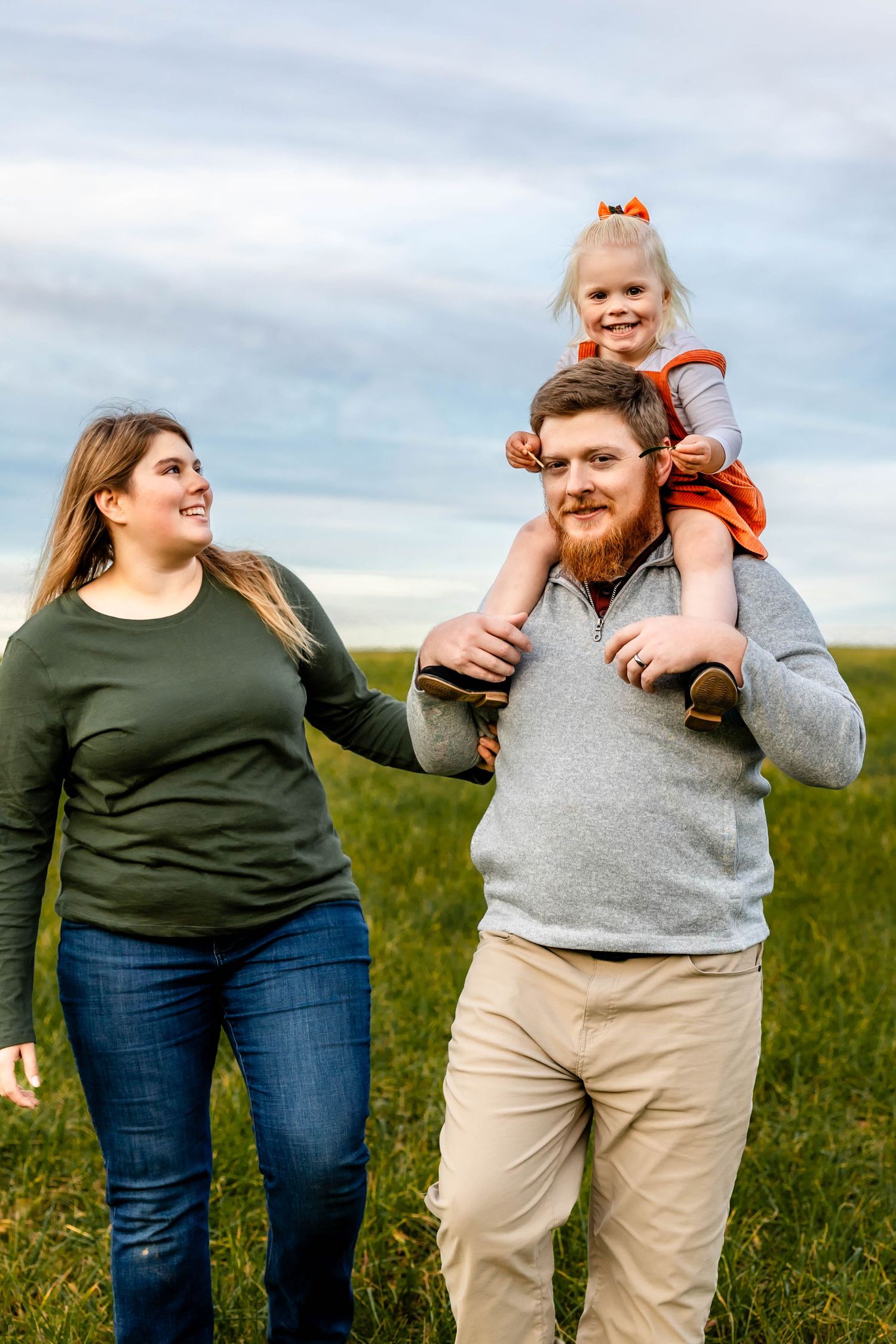 A family shares joyful moments together while standing in a green field on a cloudy day.