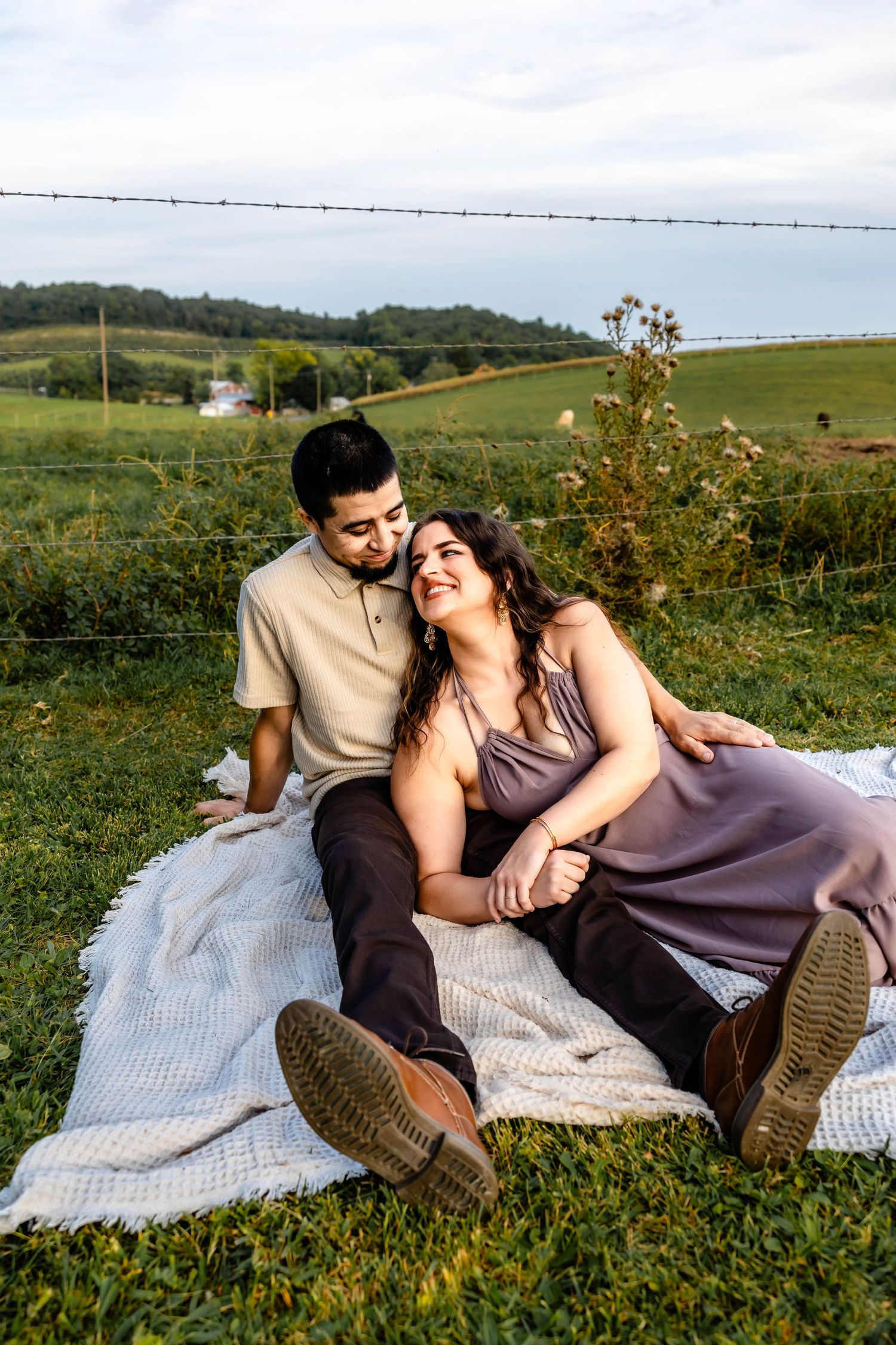 A romantic couple shares an intimate moment while lounging on a blanket in a grassy field.