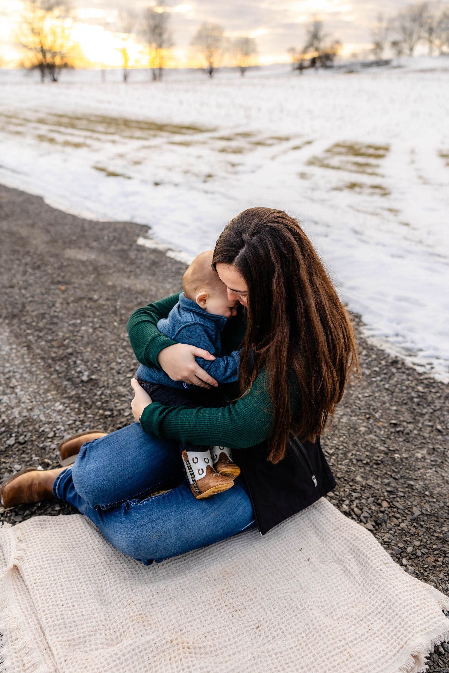 A tender moment captured on a blanket against a snowy winter landscape during sunset.
