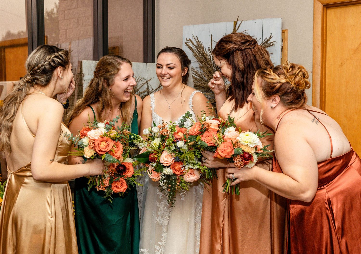 Bridal party shares laughter while holding vibrant peach and coral flower bouquets.