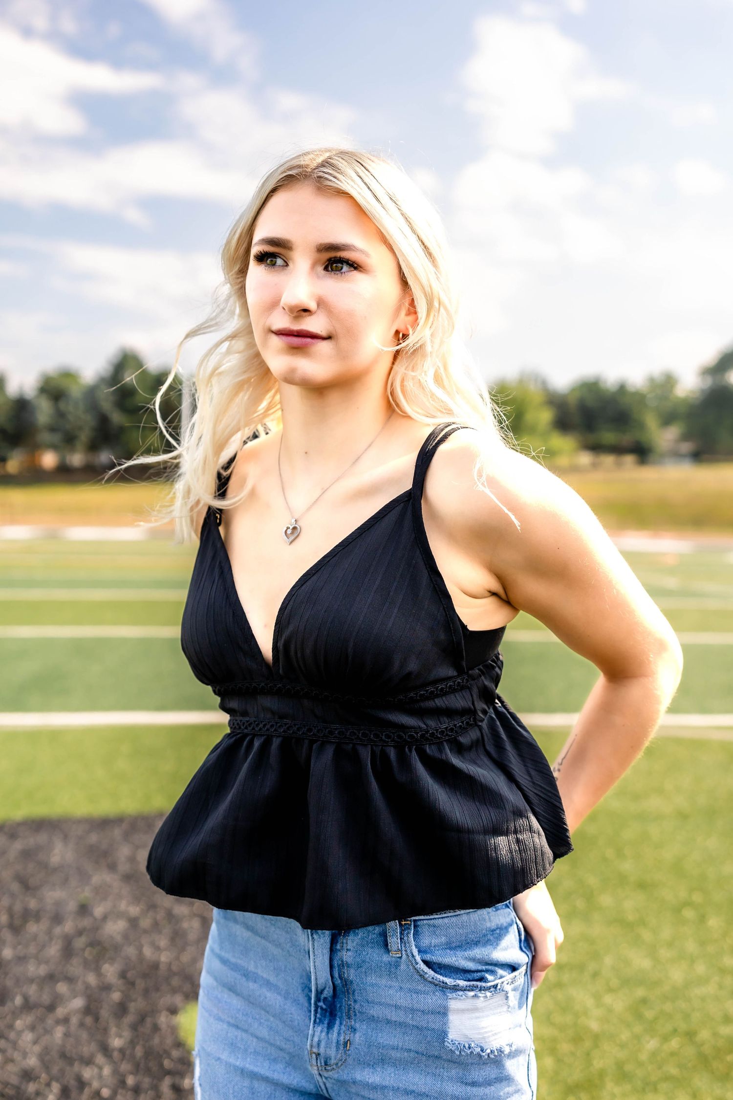 Casual summer fashion photo of a black peplum top and distressed jeans on a sports field.