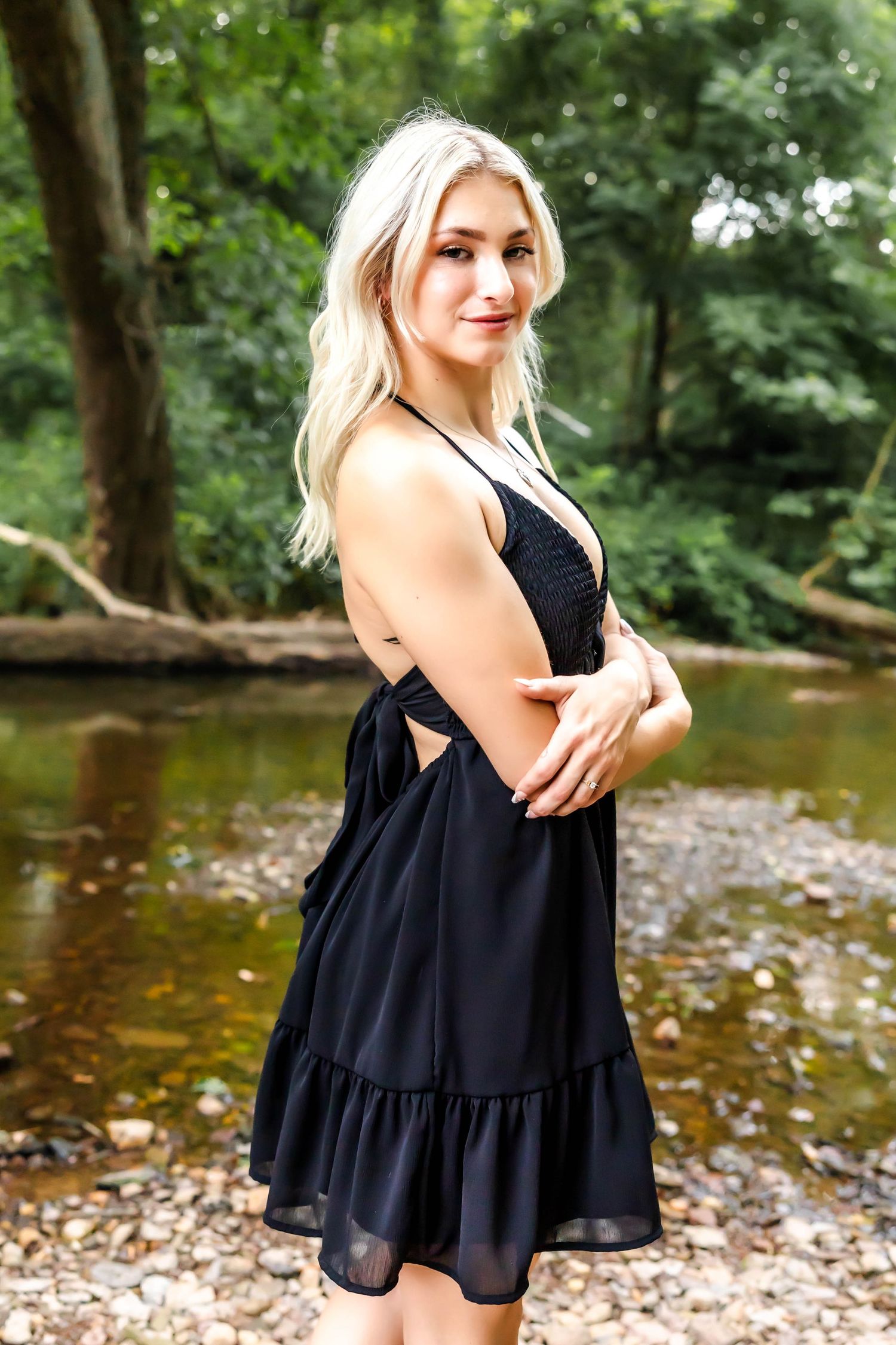 A black v-neck dress with ruffled hem photographed near a woodland stream.