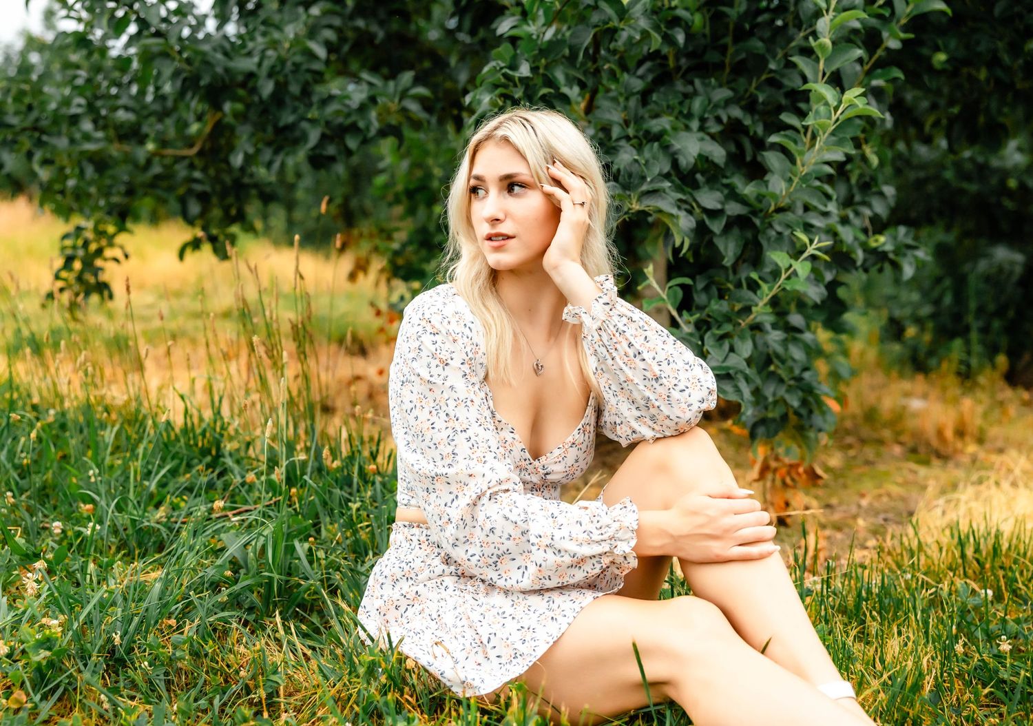 A woman in a white floral dress sits on the ground in a rustic outdoor setting.