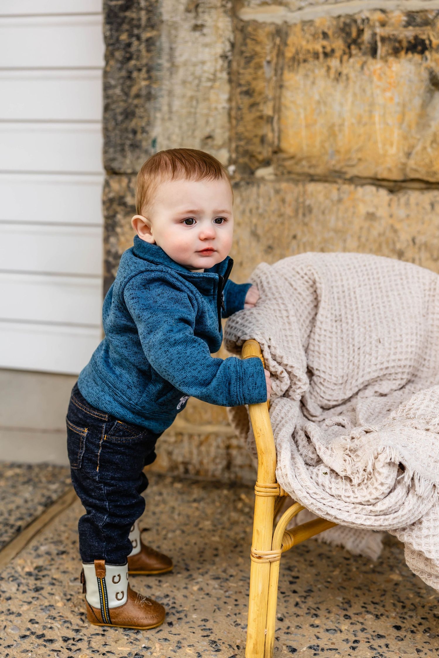 Toddler in navy sweater holding yellow chair with knit throw blanket.