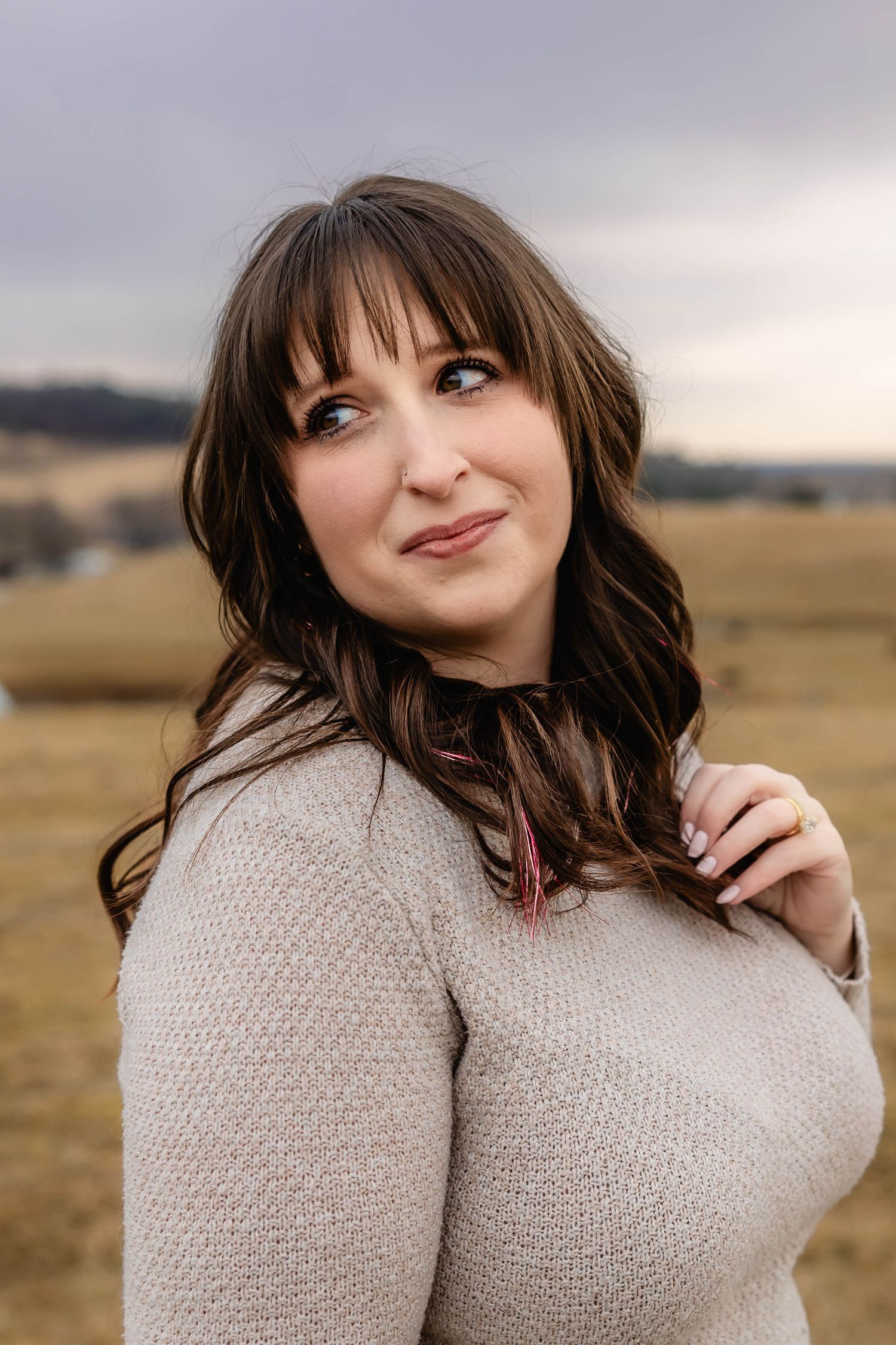 Woman in beige sweater smiling against rural autumn landscape.