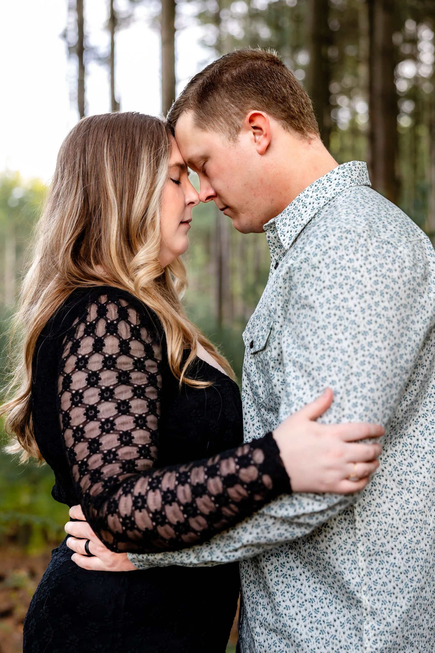 Intimate portrait of a couple in black and gray attire sharing a close moment in the woods.