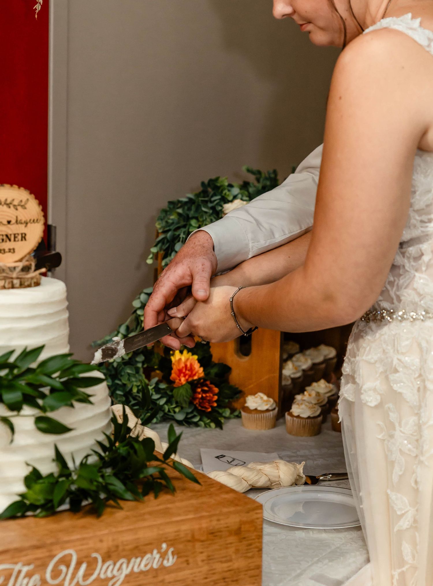 A close-up shot of hands cutting a white wedding cake adorned with greenery.
