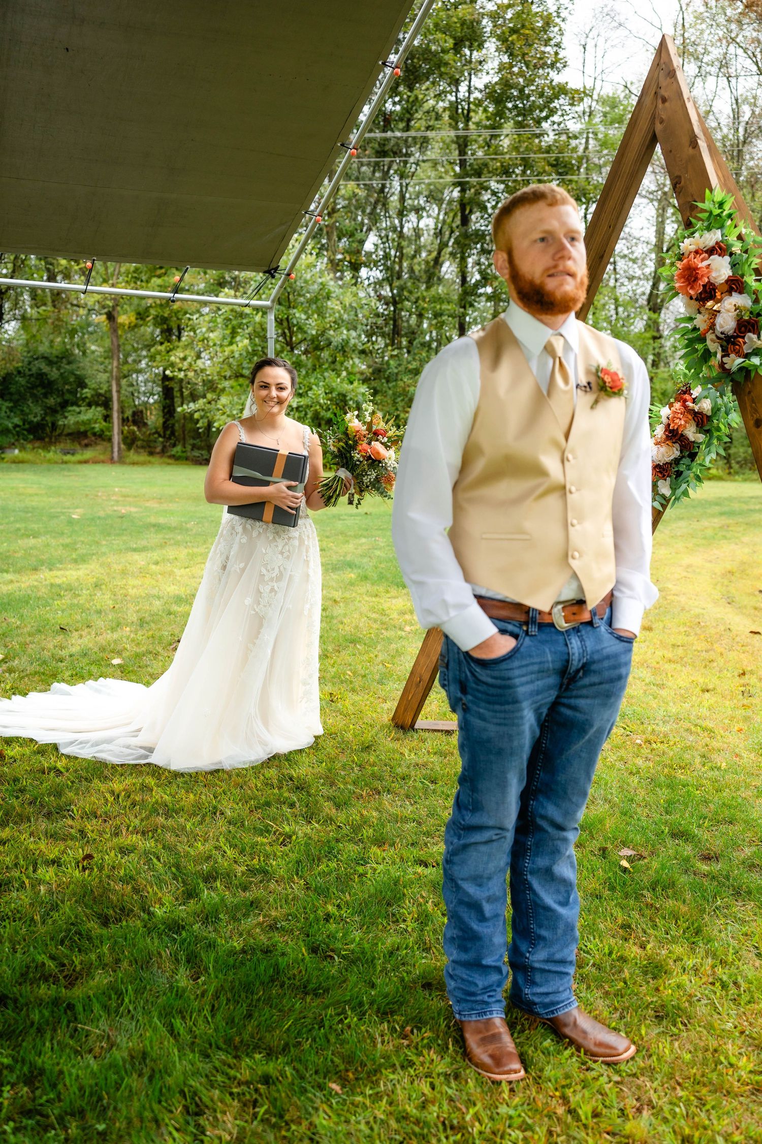 Outdoor wedding scene with a wooden triangle arch and floral decorations in a natural setting.