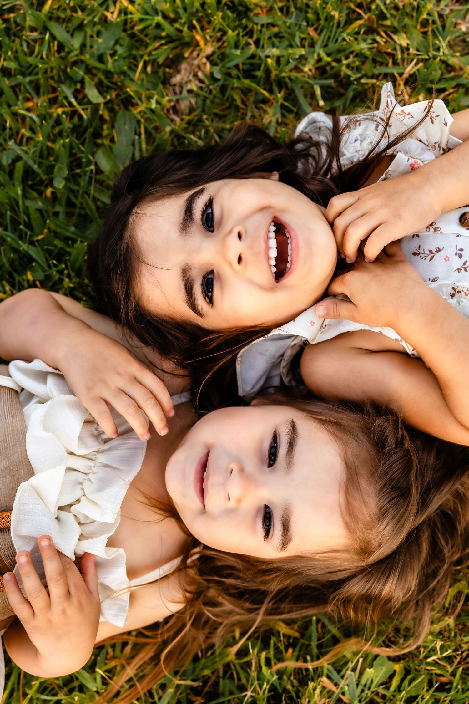 Two people lying in green grass sharing laughter and smiles while wearing floral outfits.