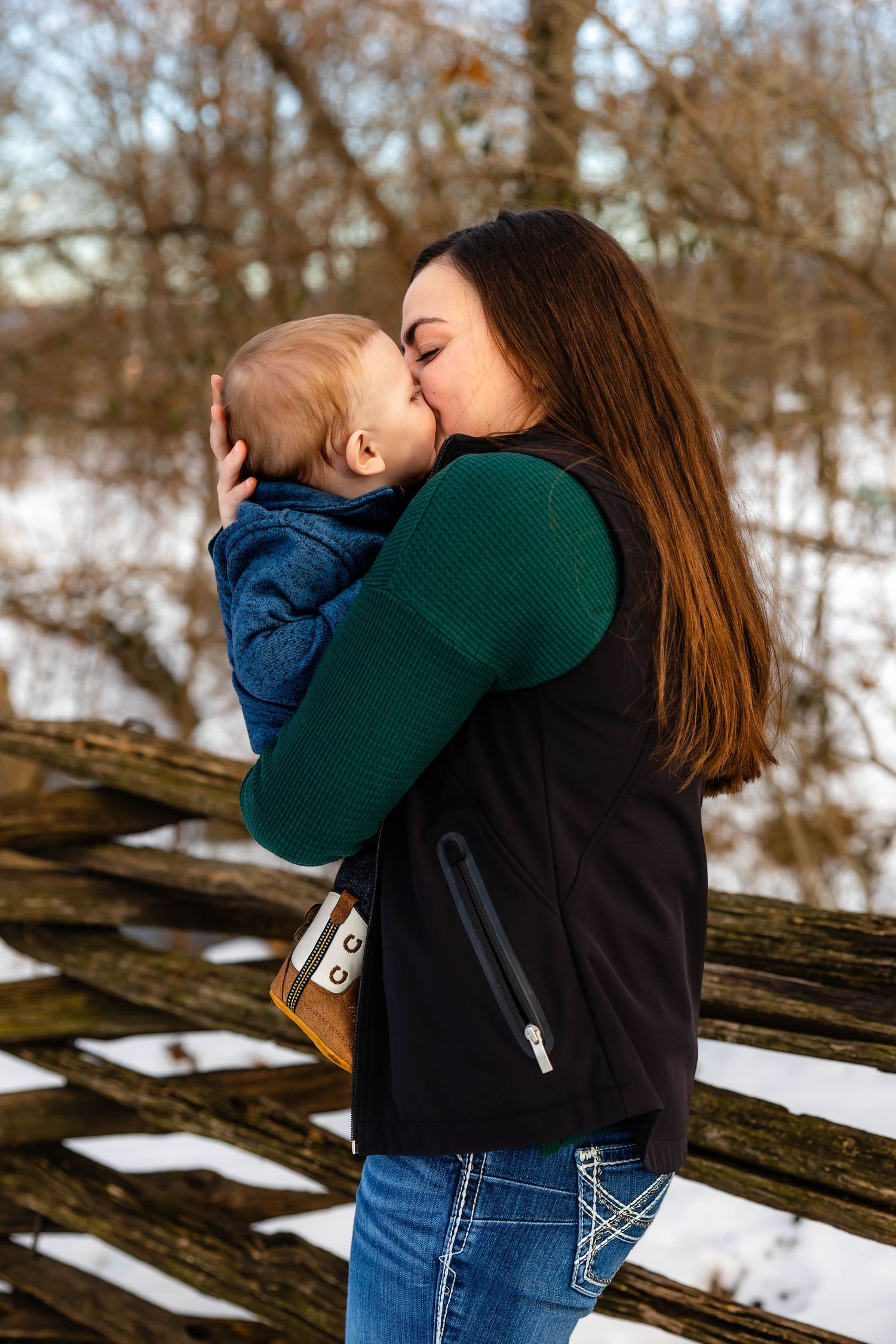 A tender embrace between parent and child against a snowy winter backdrop with wooden fence.