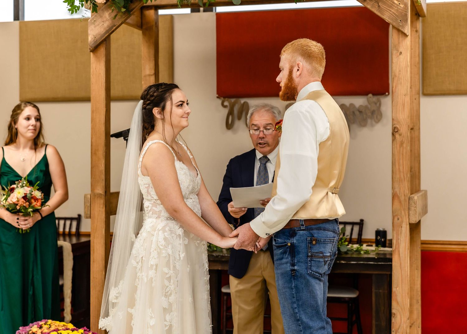 A wedding ceremony taking place under a wooden arch with attendants in emerald green.