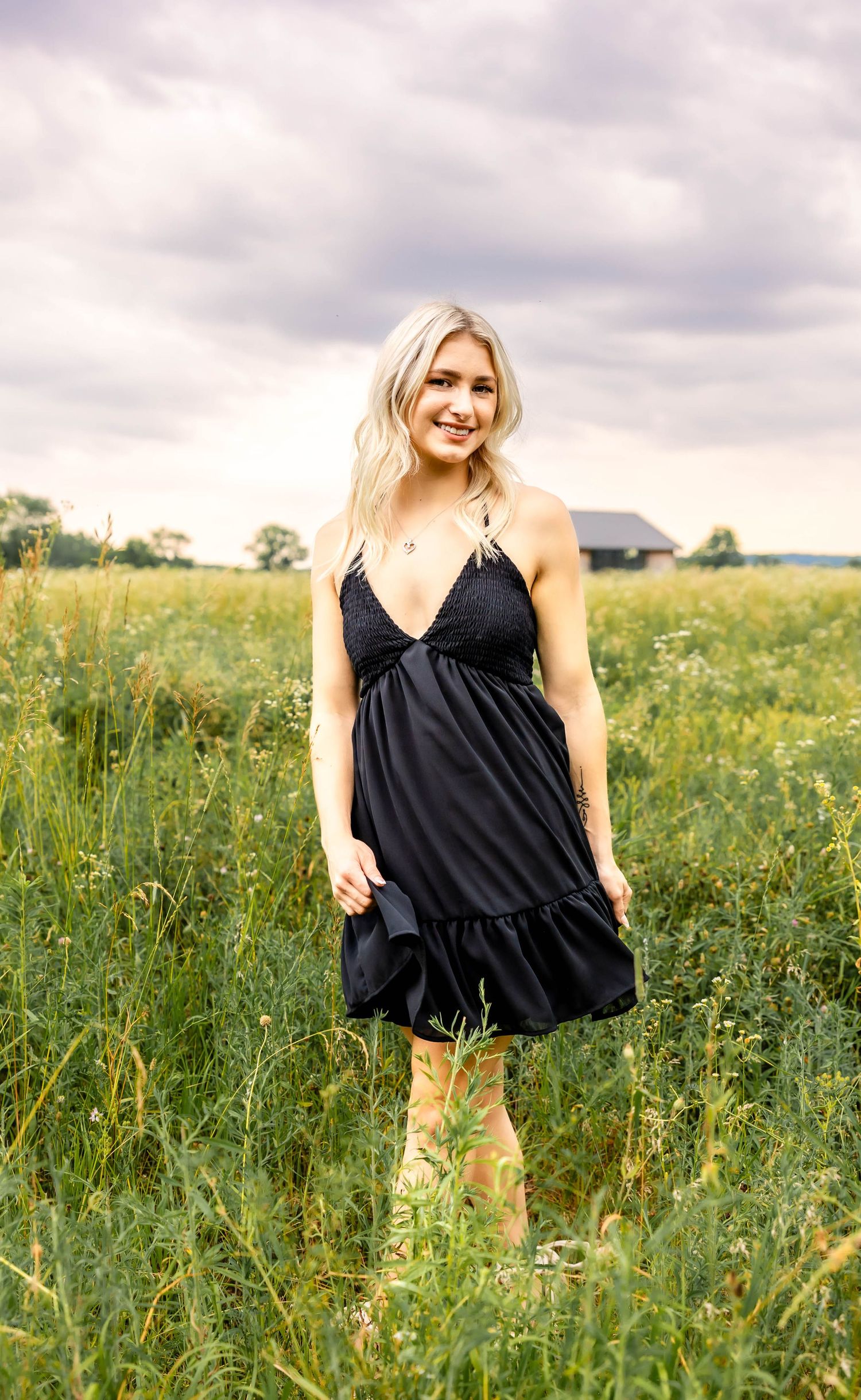 A black sundress with ruffled hem photographed in a sunny wildflower meadow with cloudy sky.