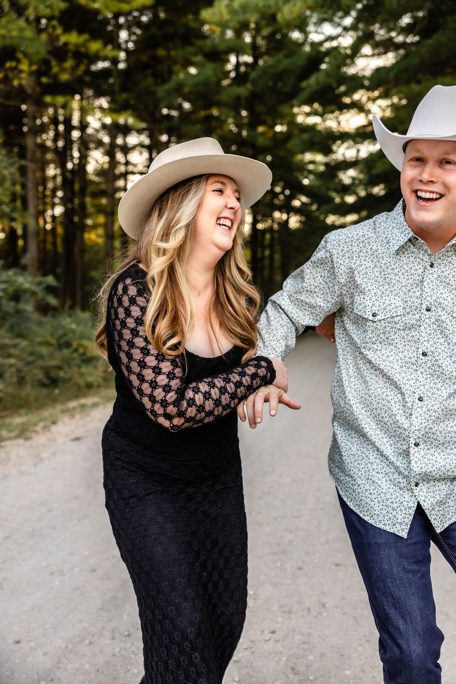A couple enjoying a lighthearted moment together on a wooded trail, wearing matching cowboy hats.